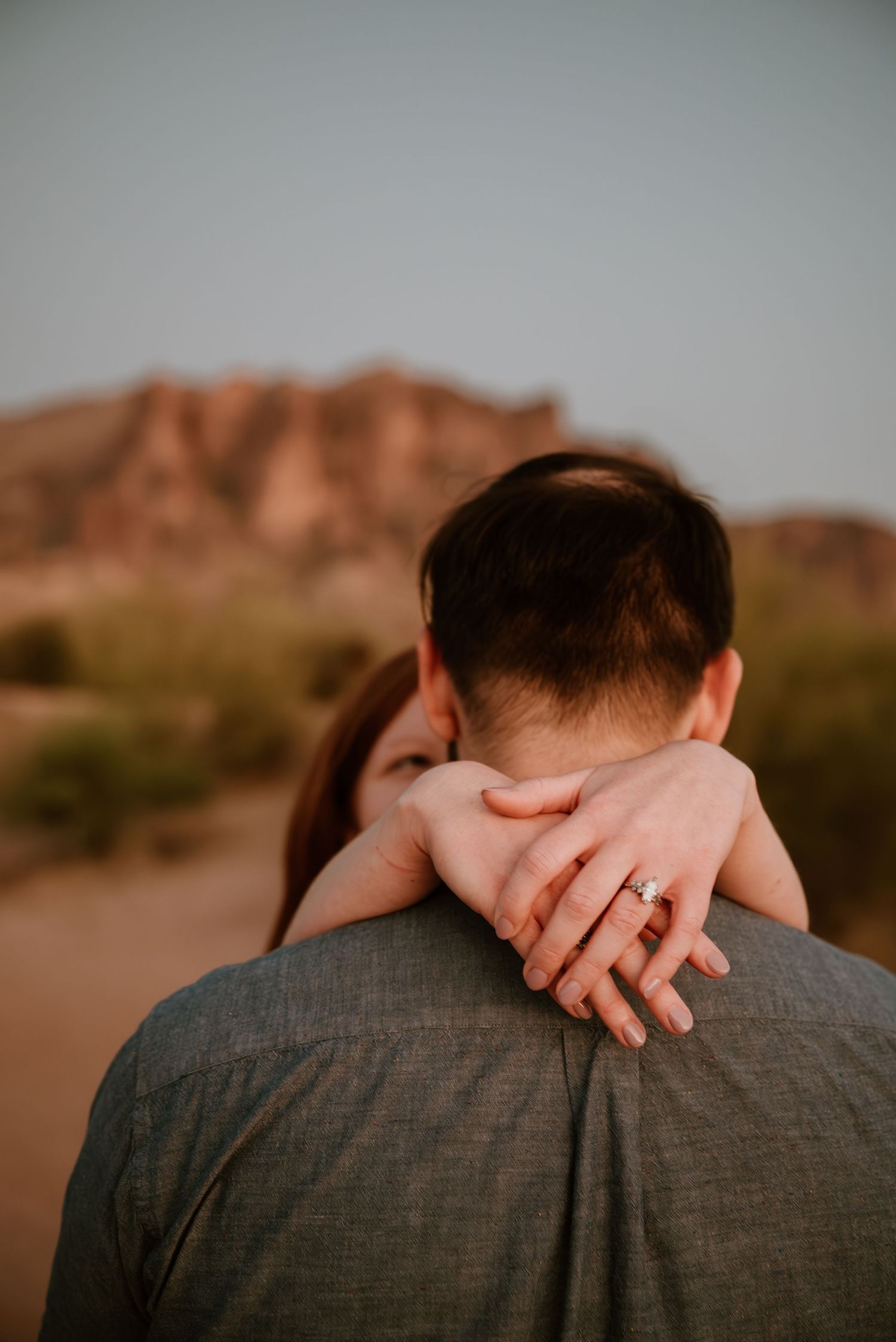 Close-up desert portrait showing hand resting on shoulder against mountain backdrop.
