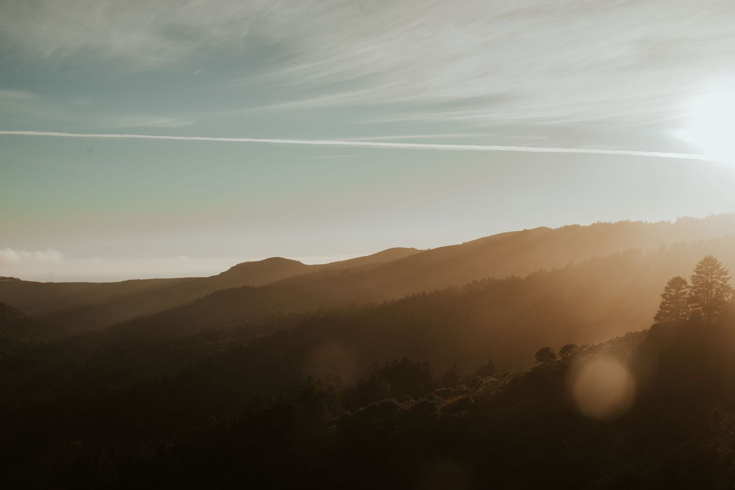 Golden sunset light illuminates rolling hills against a hazy sky.