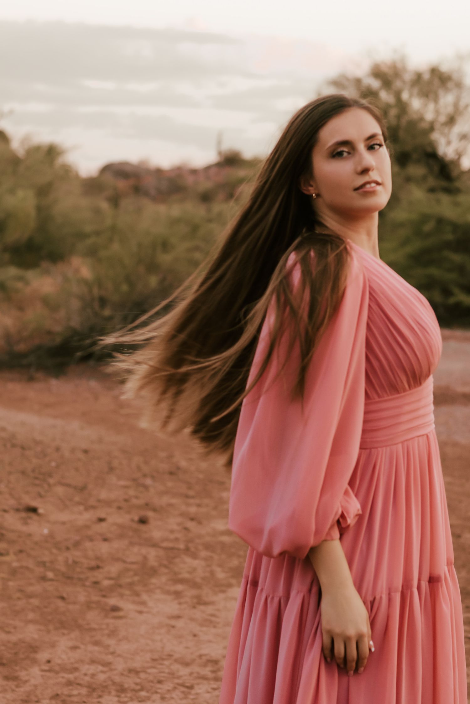 Pink dress flows in the wind during desert photoshoot at sunset.