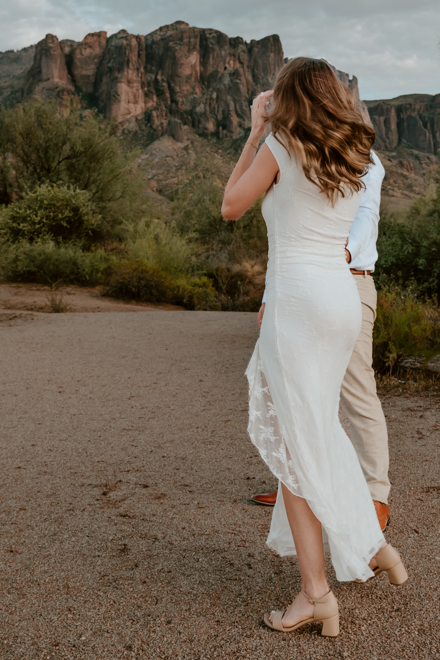 Couple embracing in white wedding attire with stunning desert mountain backdrop in Arizona.