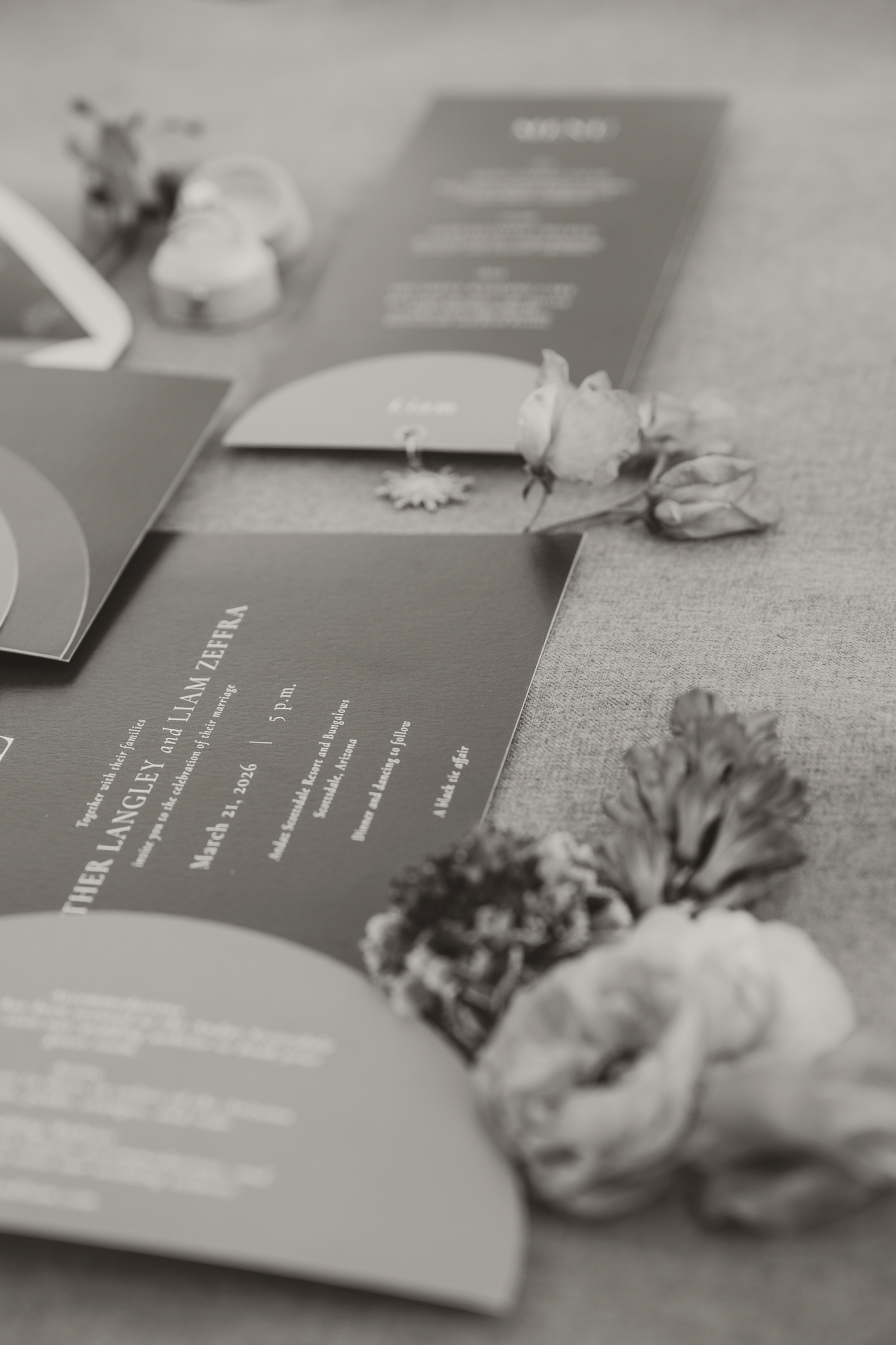 Black and white photo of elegant wedding invitation suite with floral accents arranged on a table.
