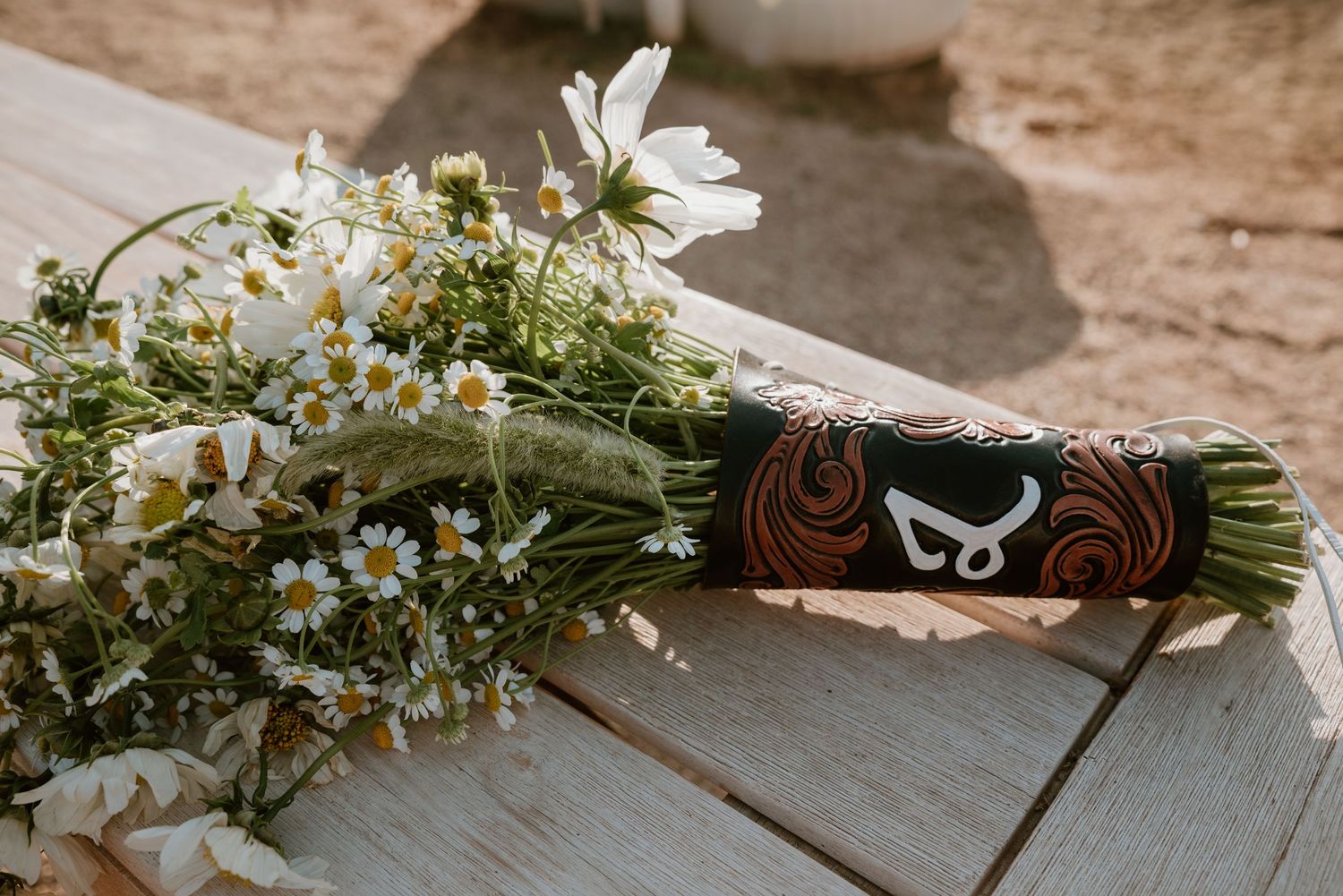 Rustic floral arrangement of white daisies and greenery laid on wooden surface.