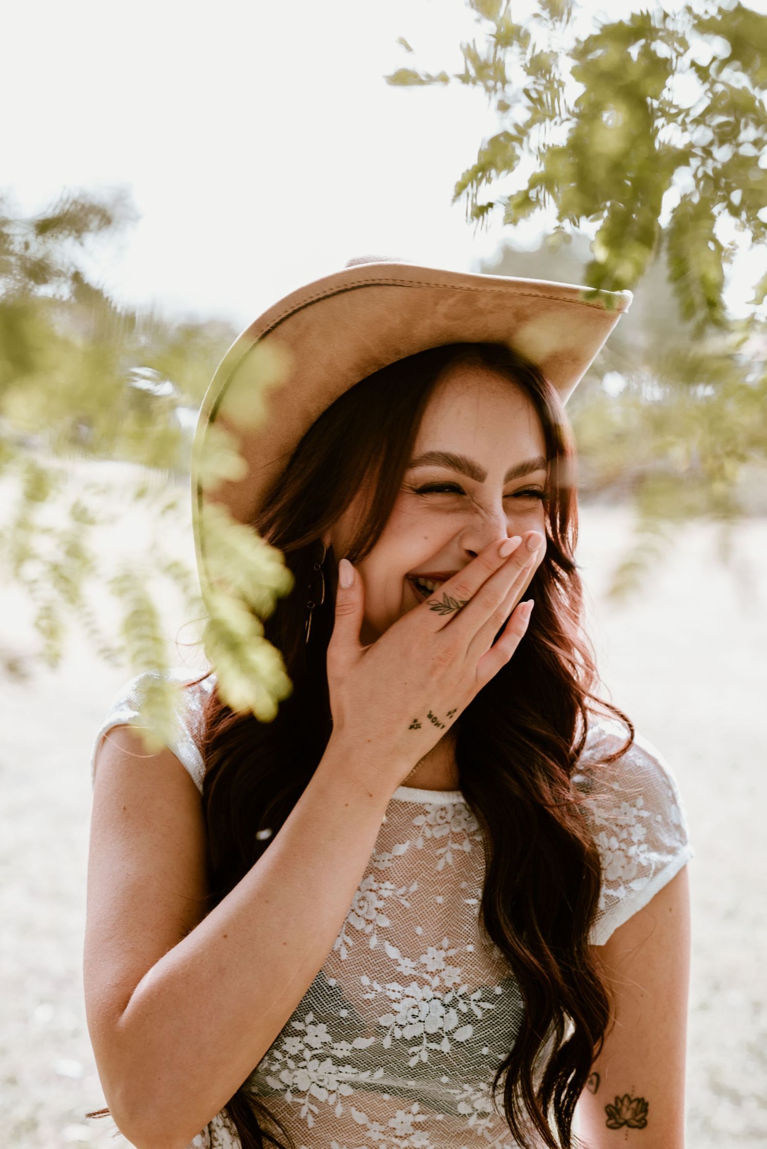 A joyful candid moment in a lace top and brown cowboy hat against a soft bokeh background.