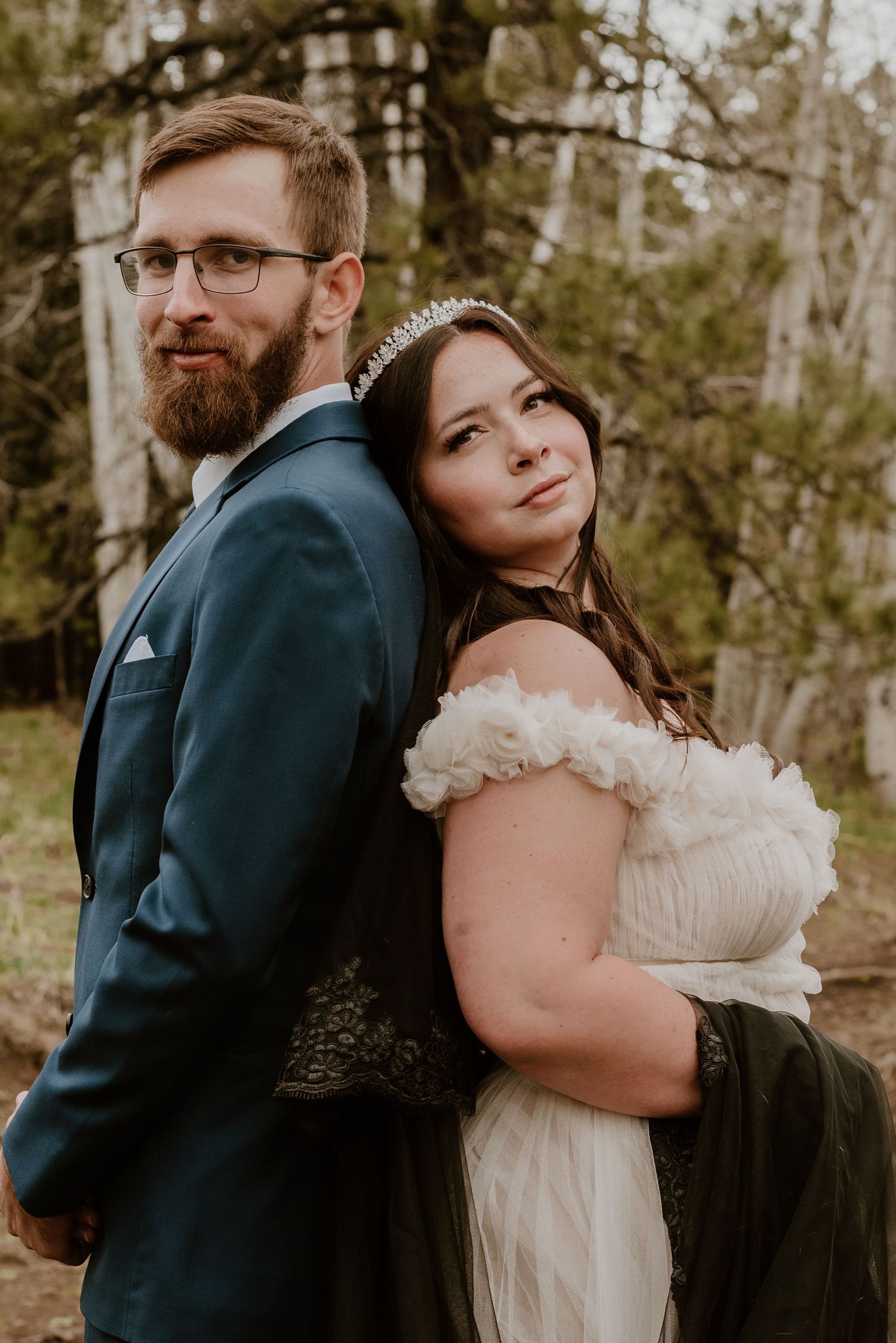 A rustic outdoor wedding portrait featuring elegant formal attire against a natural forest backdrop.