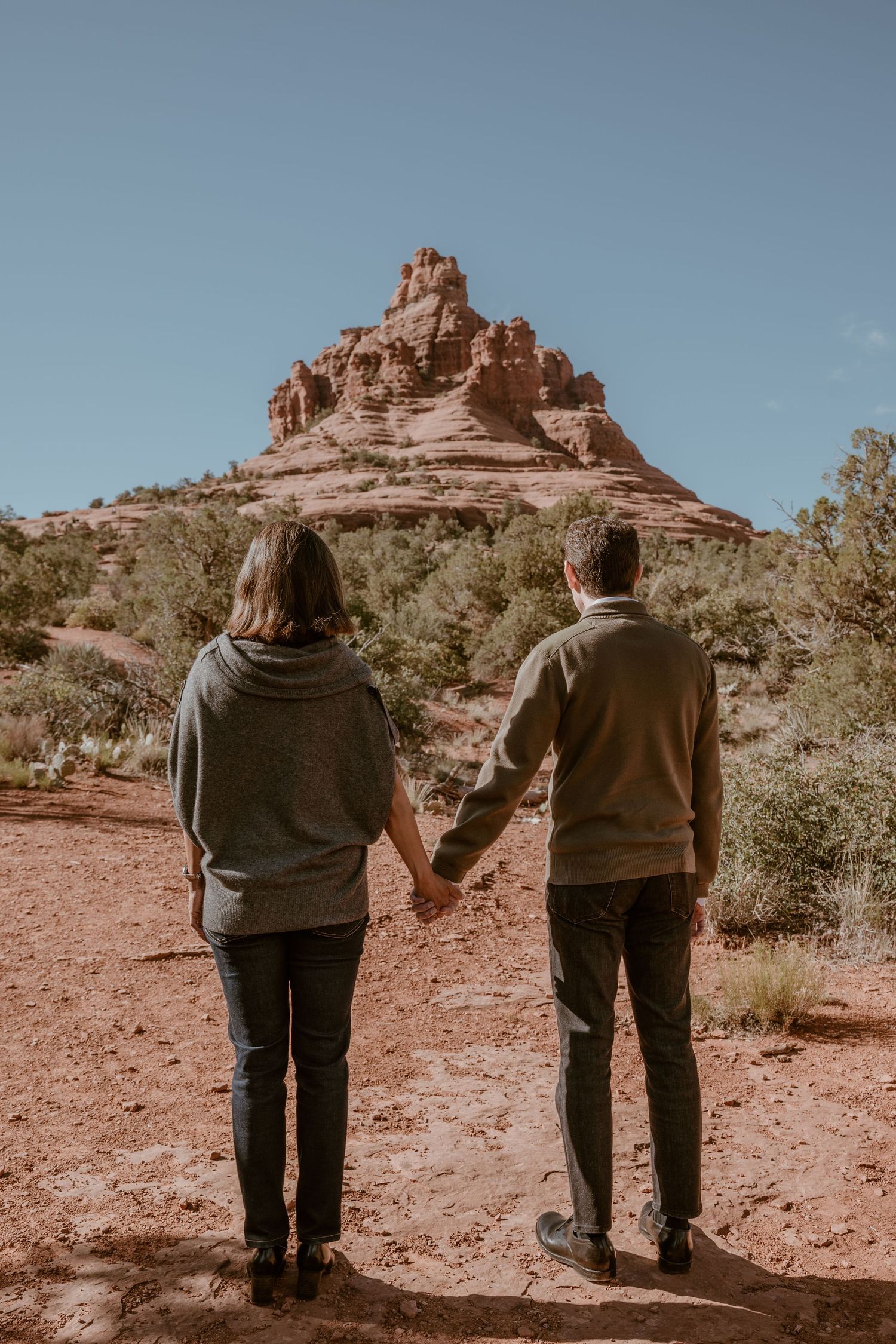 Backs of two people standing together against desert mountain landscape.