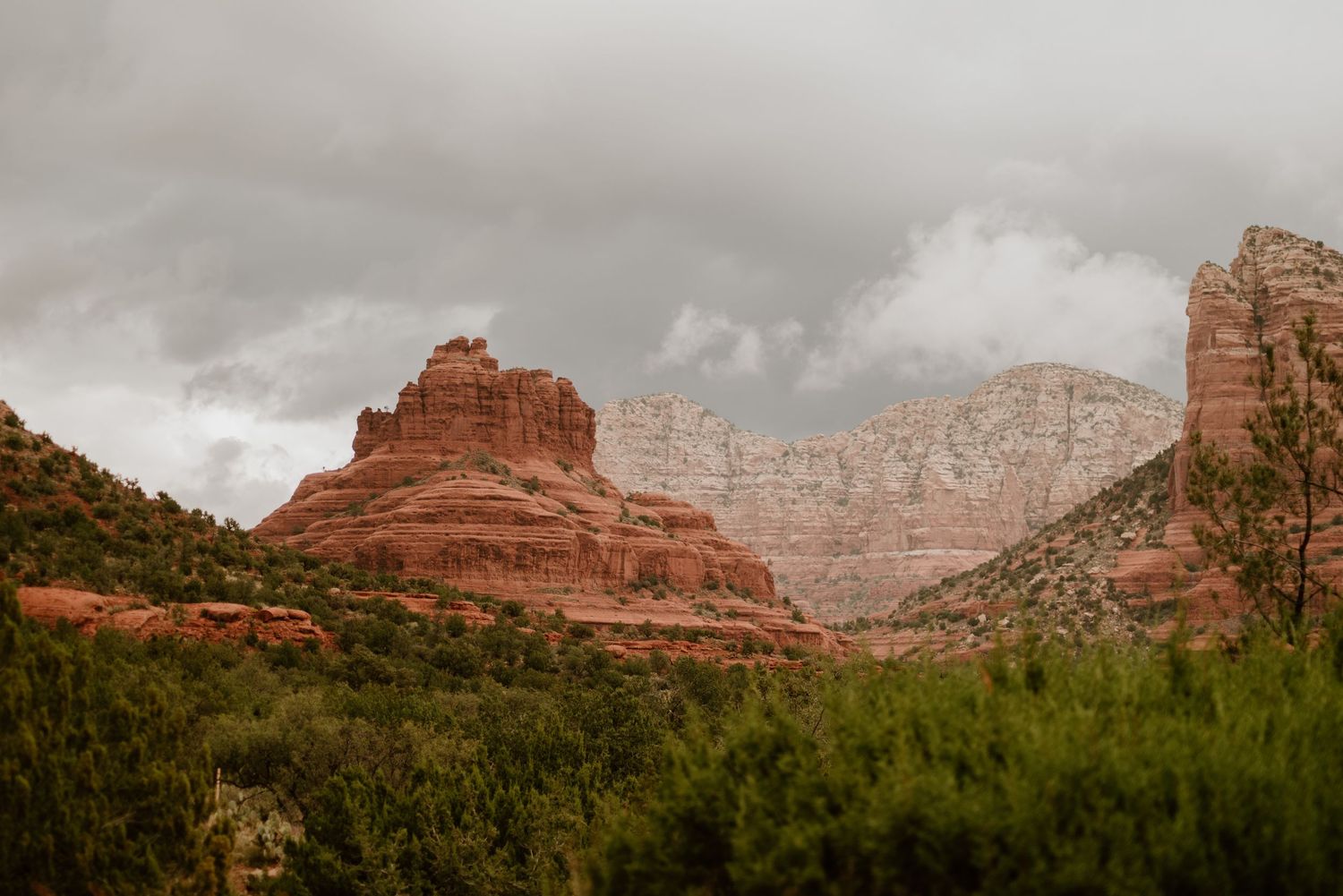 Red rock formations rise dramatically against cloudy skies in Sedona's desert landscape.