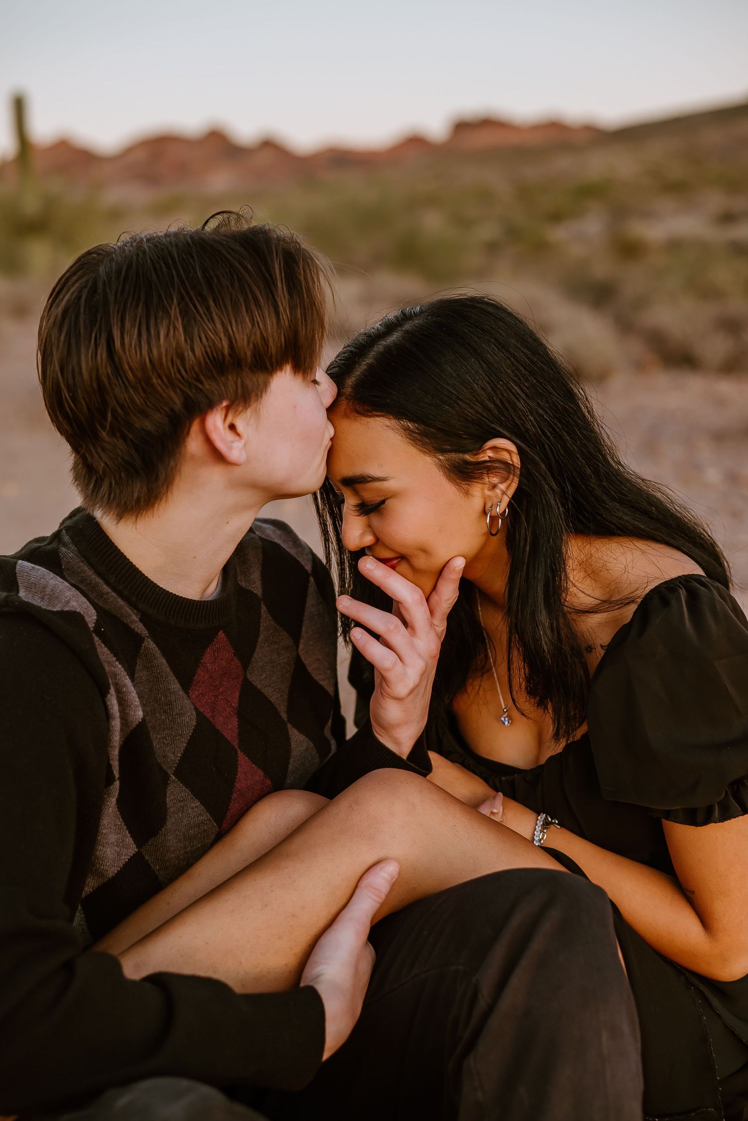 A romantic sunset moment between two people laughing and embracing in desert scenery.