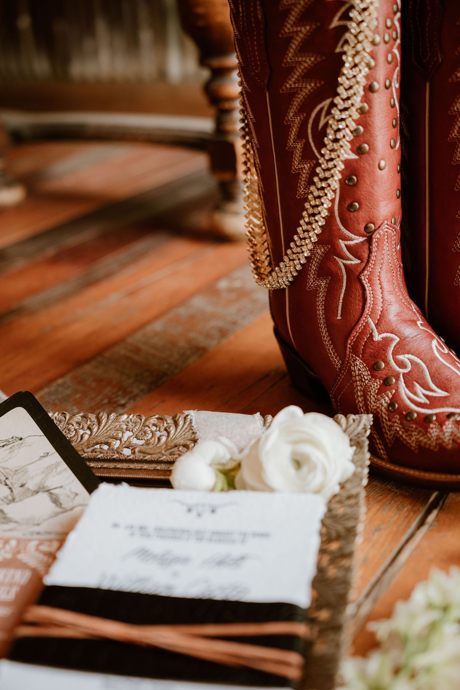 Decorated brown leather cowboy boots with white flowers and wedding invitation details.