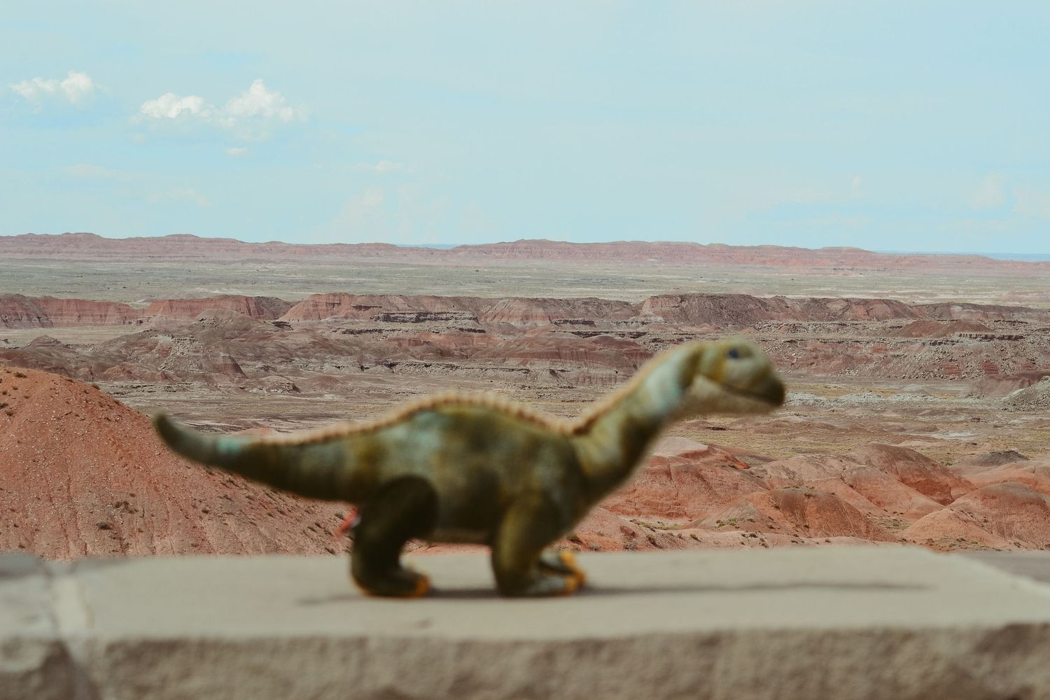 Miniature dinosaur figurines displayed against a desert landscape backdrop.