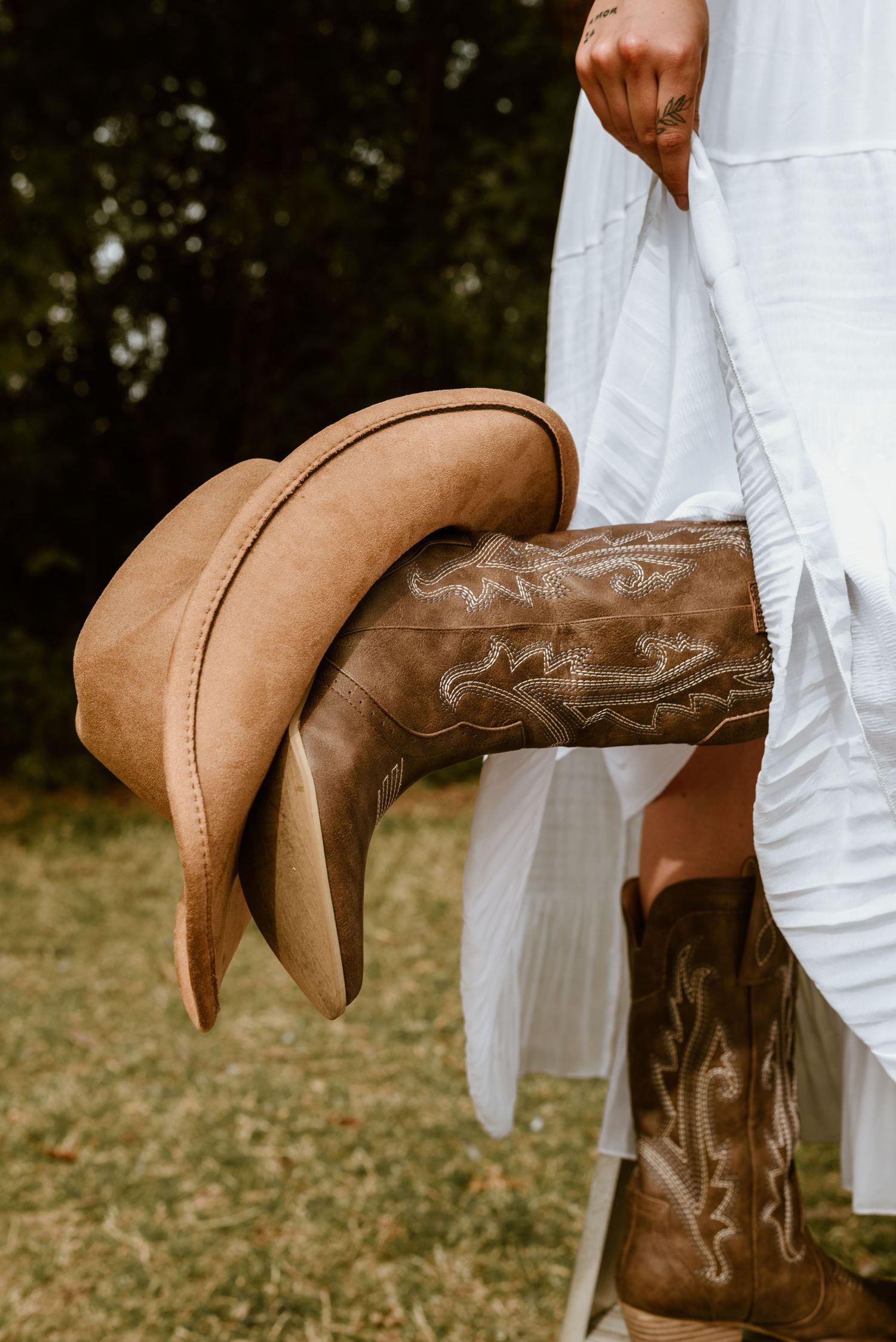 Brown leather cowboy boots shown against white dress in outdoor setting.