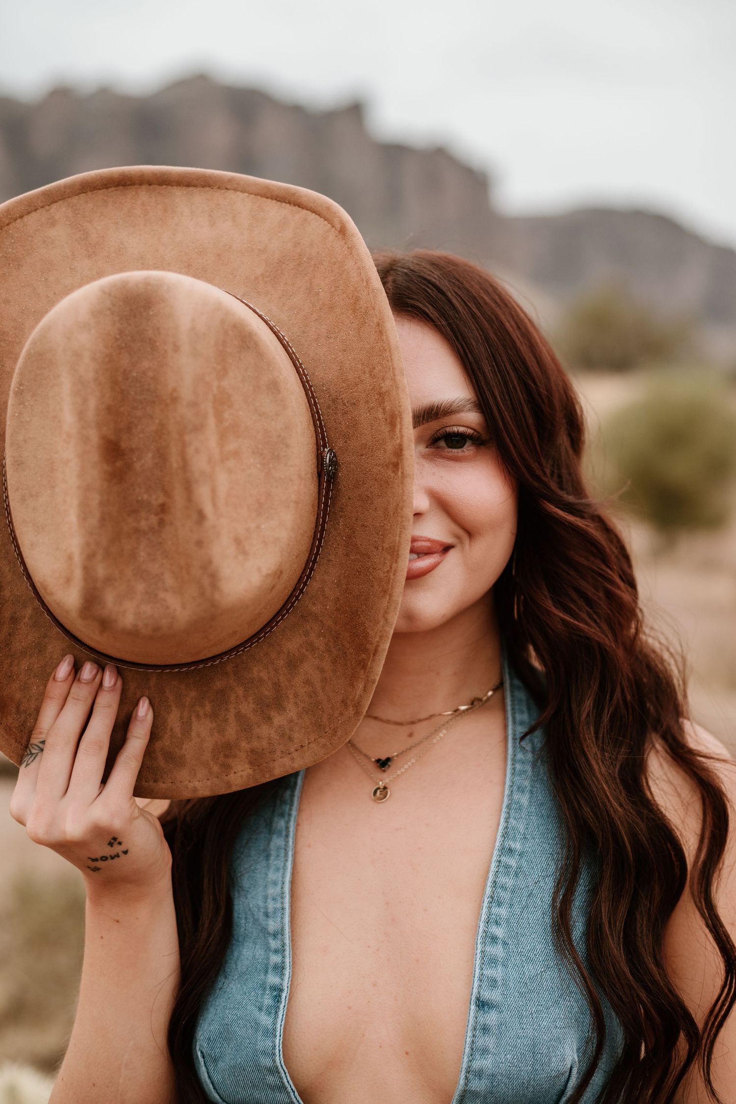 Playful portrait of someone peeking behind a brown suede hat wearing denim.