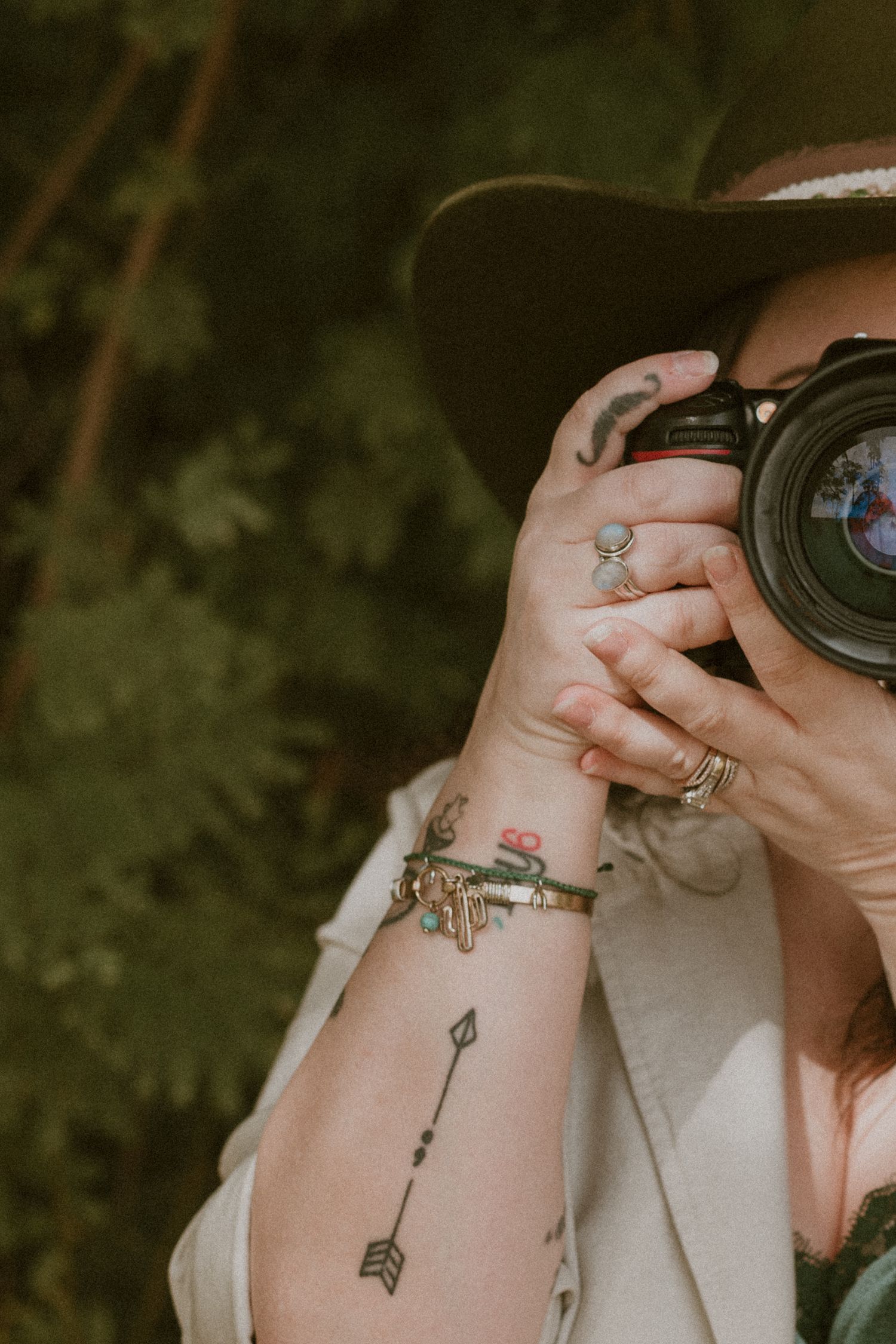 Close-up of hands holding camera with arrow tattoo visible on wrist.