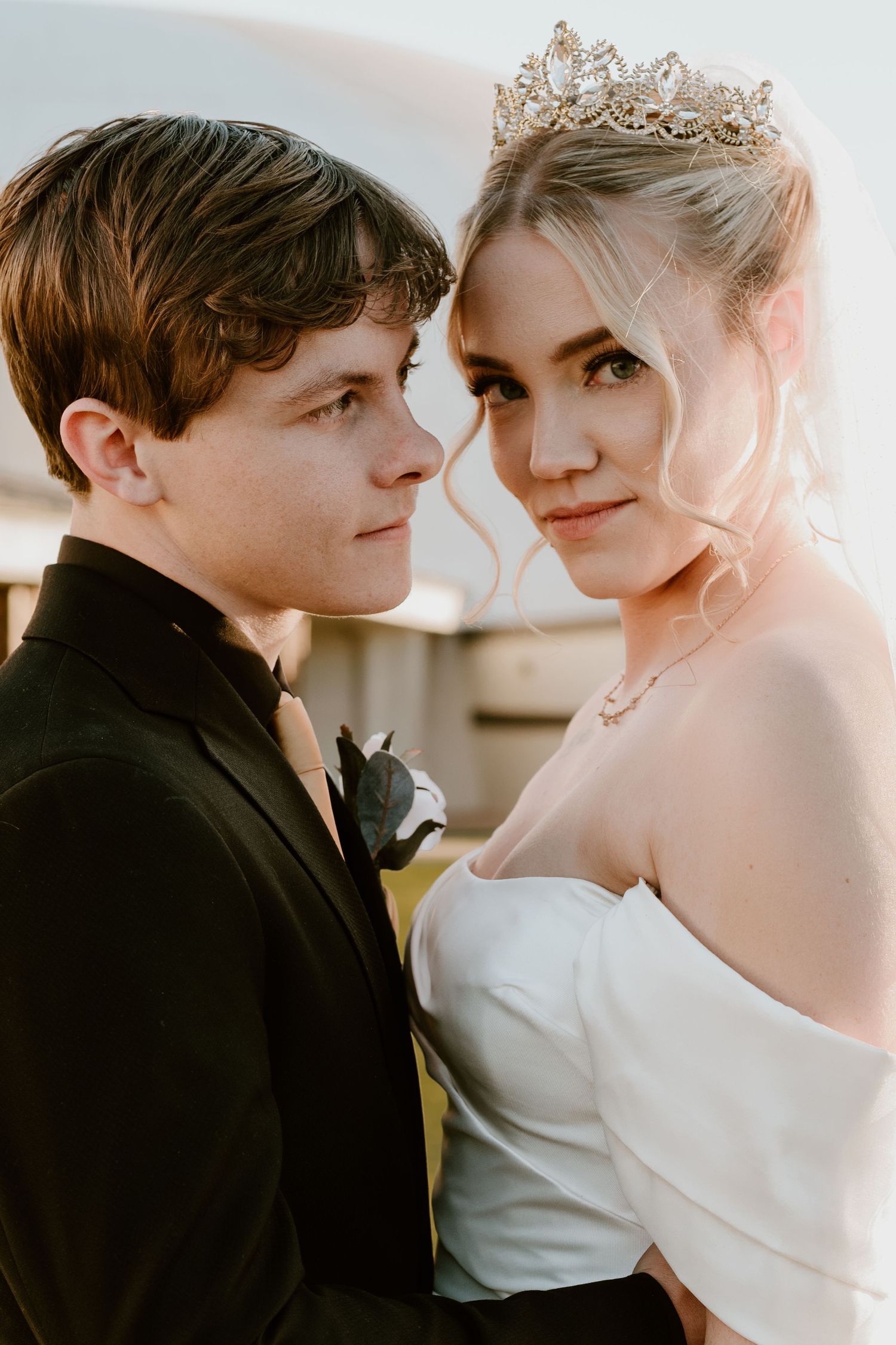A close-up wedding portrait showcasing elegant bridal attire including a tiara and classic black tuxedo.