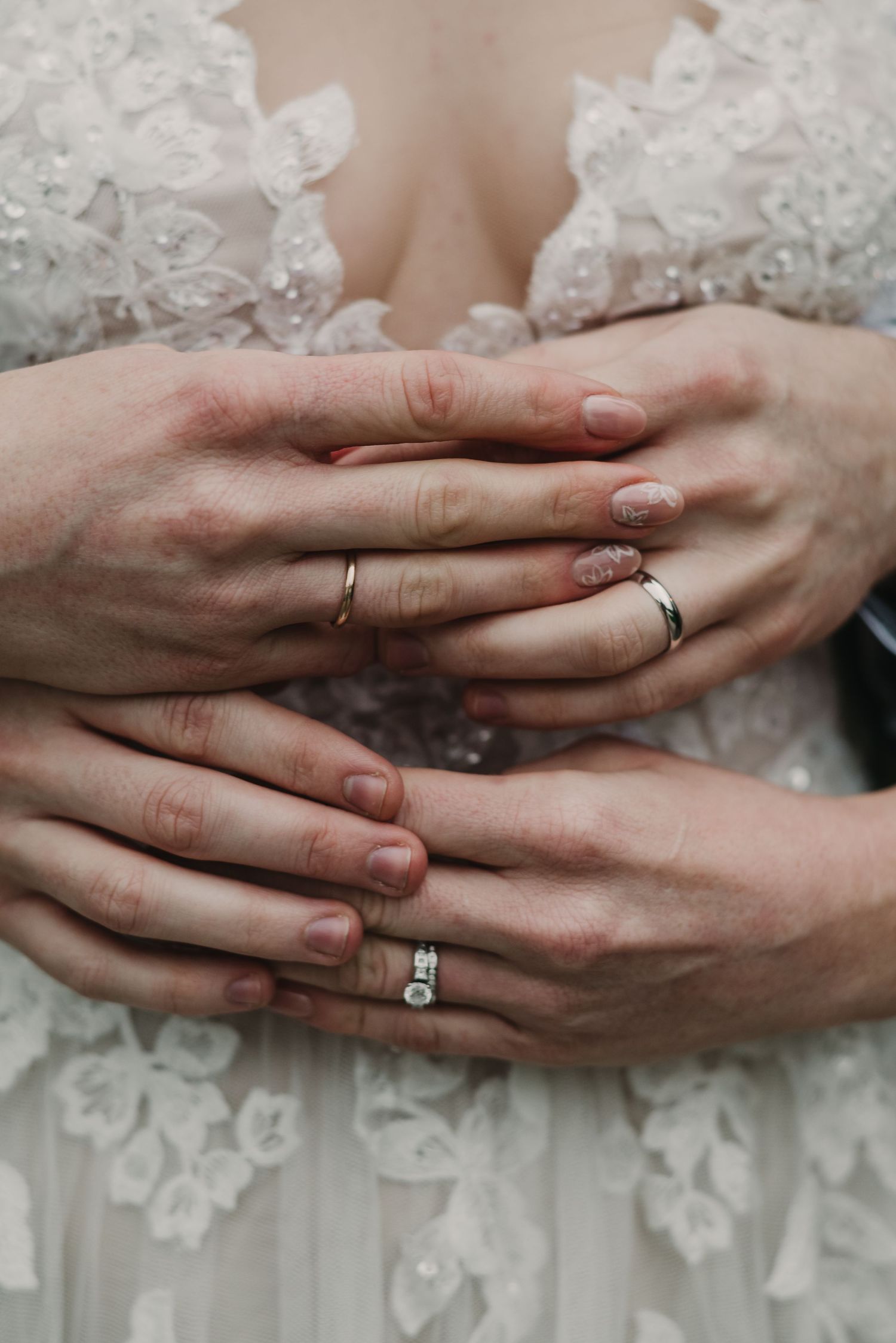 Close-up of hands wearing wedding rings against a detailed white lace dress.