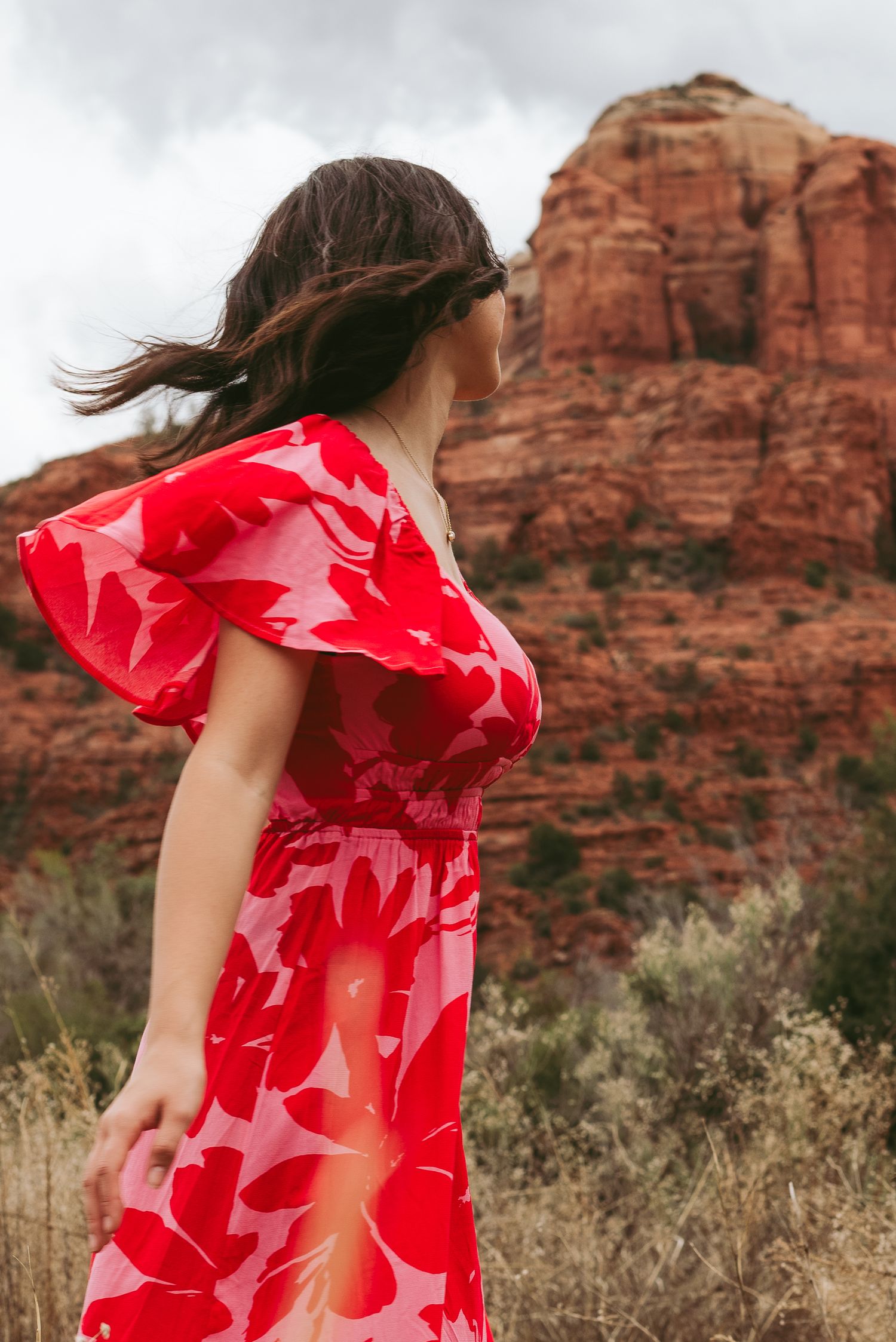 Red floral dress flowing in the wind against dramatic red rock formations.