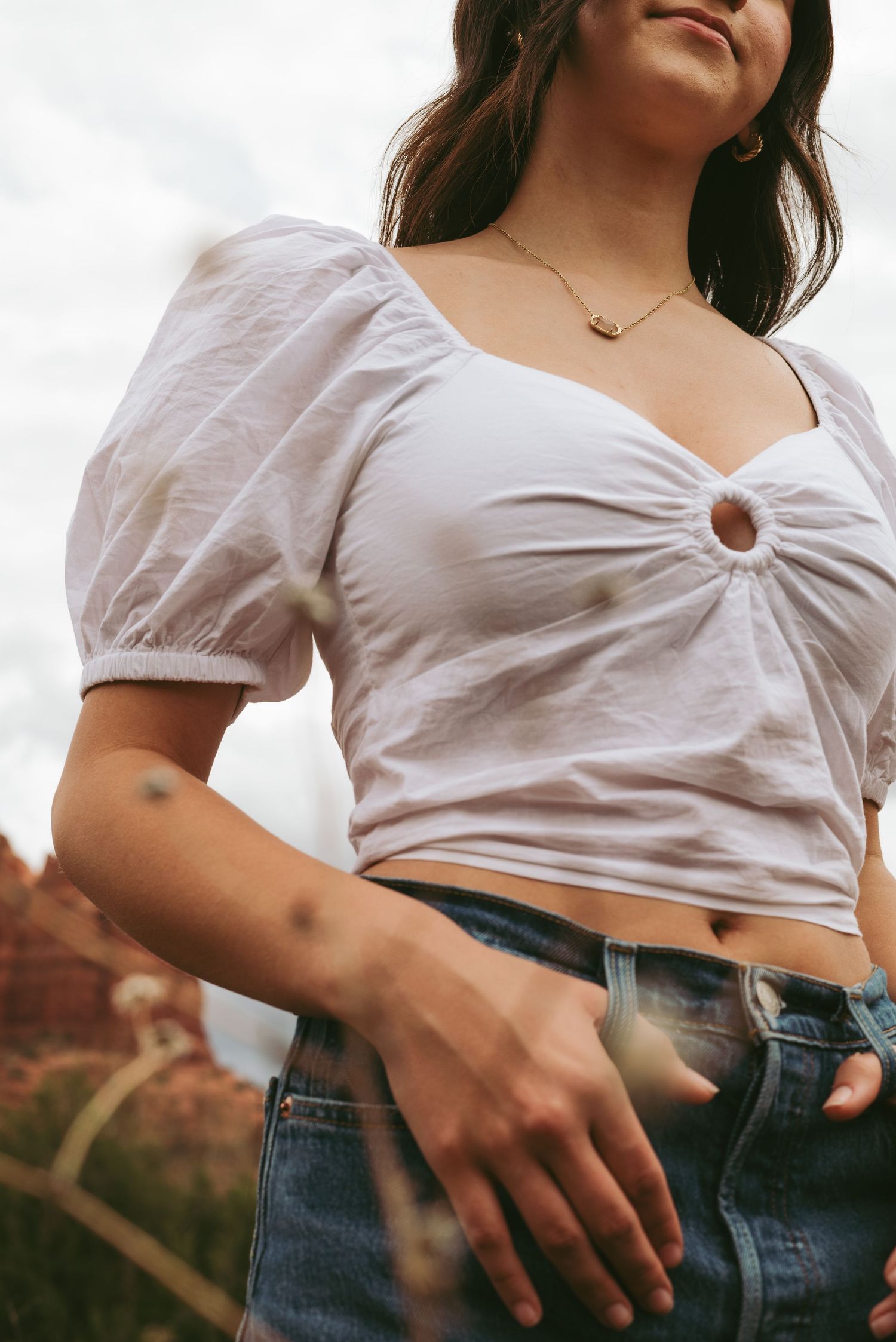 Close-up of white puff sleeve crop top and denim jeans with jewelry accents.