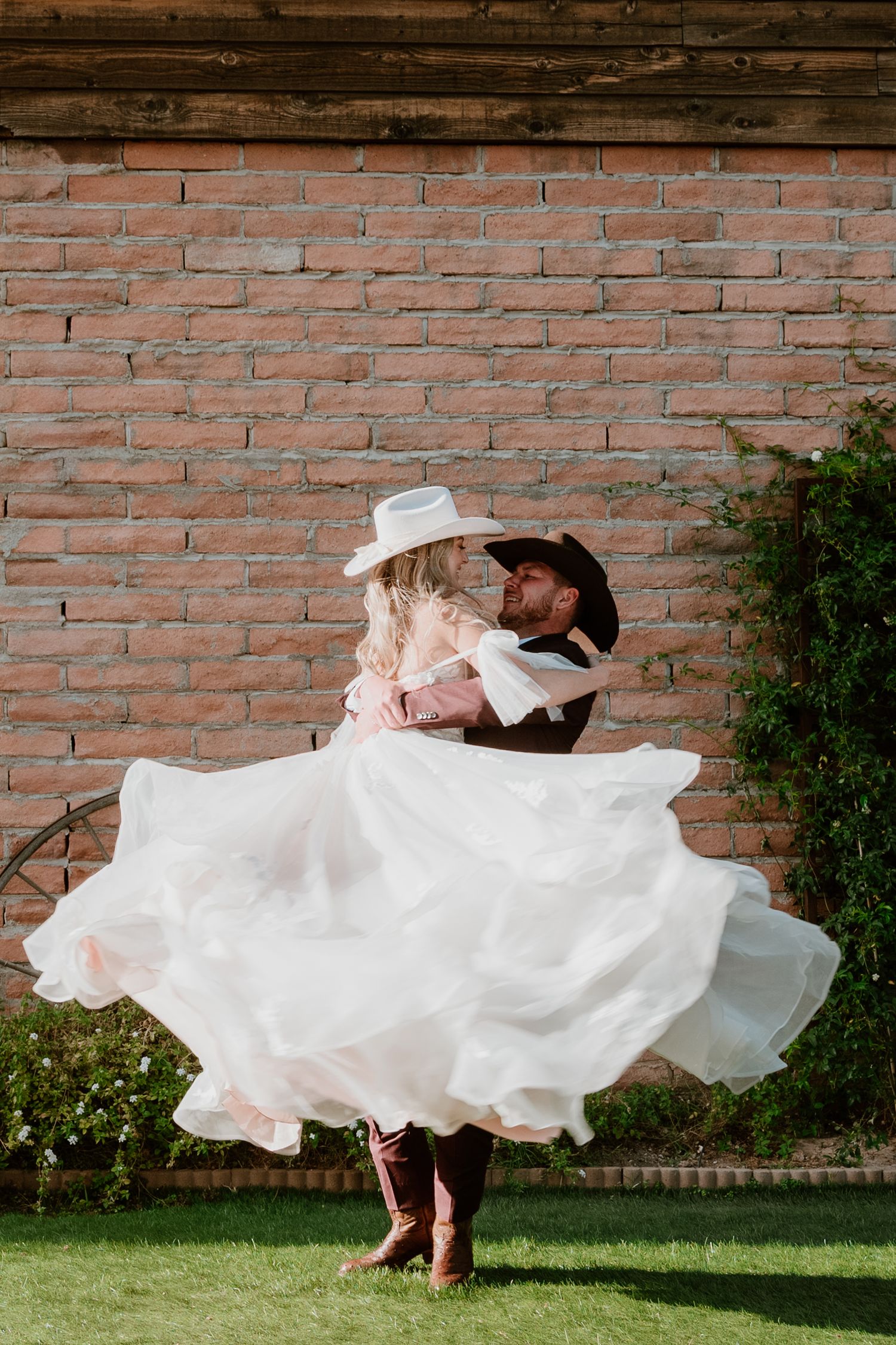 Flowing white dress twirling against brick wall in outdoor garden setting.
