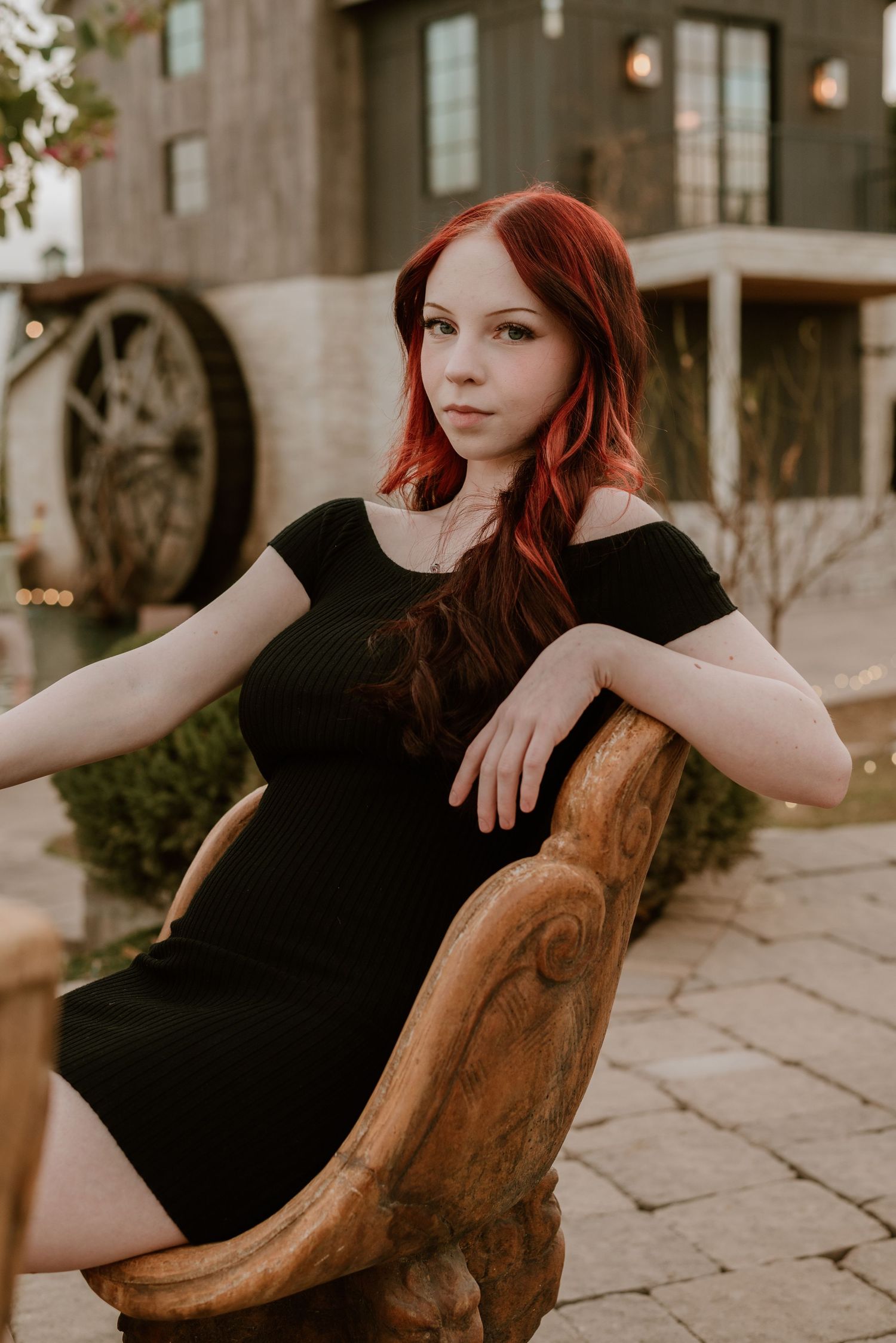 Elegant pose in black dress on wooden outdoor furniture.