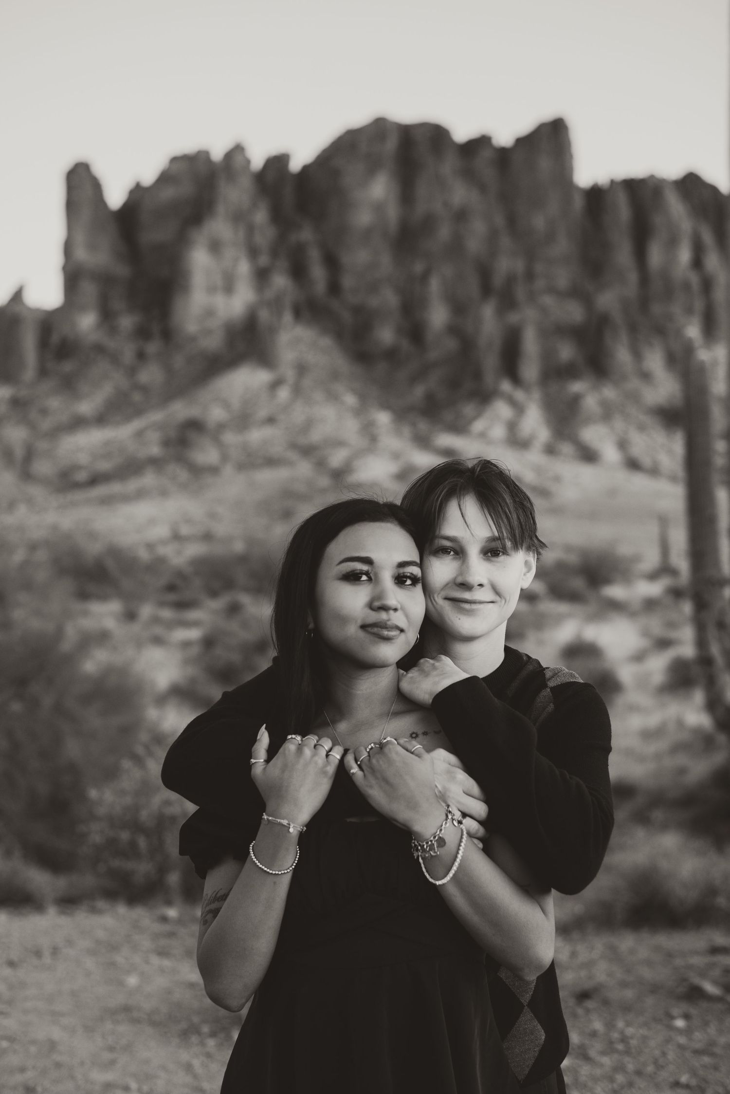 A couple embraces in black clothing with scenic desert mountains in the background.