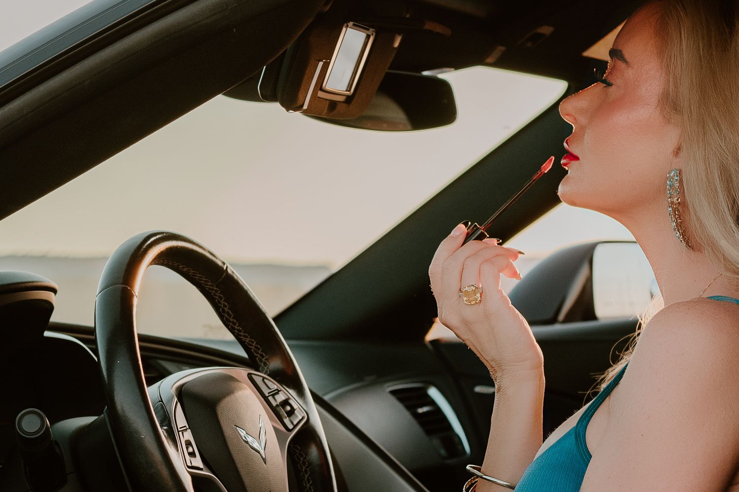 Woman applying lipstick and checking makeup in car rearview mirror.