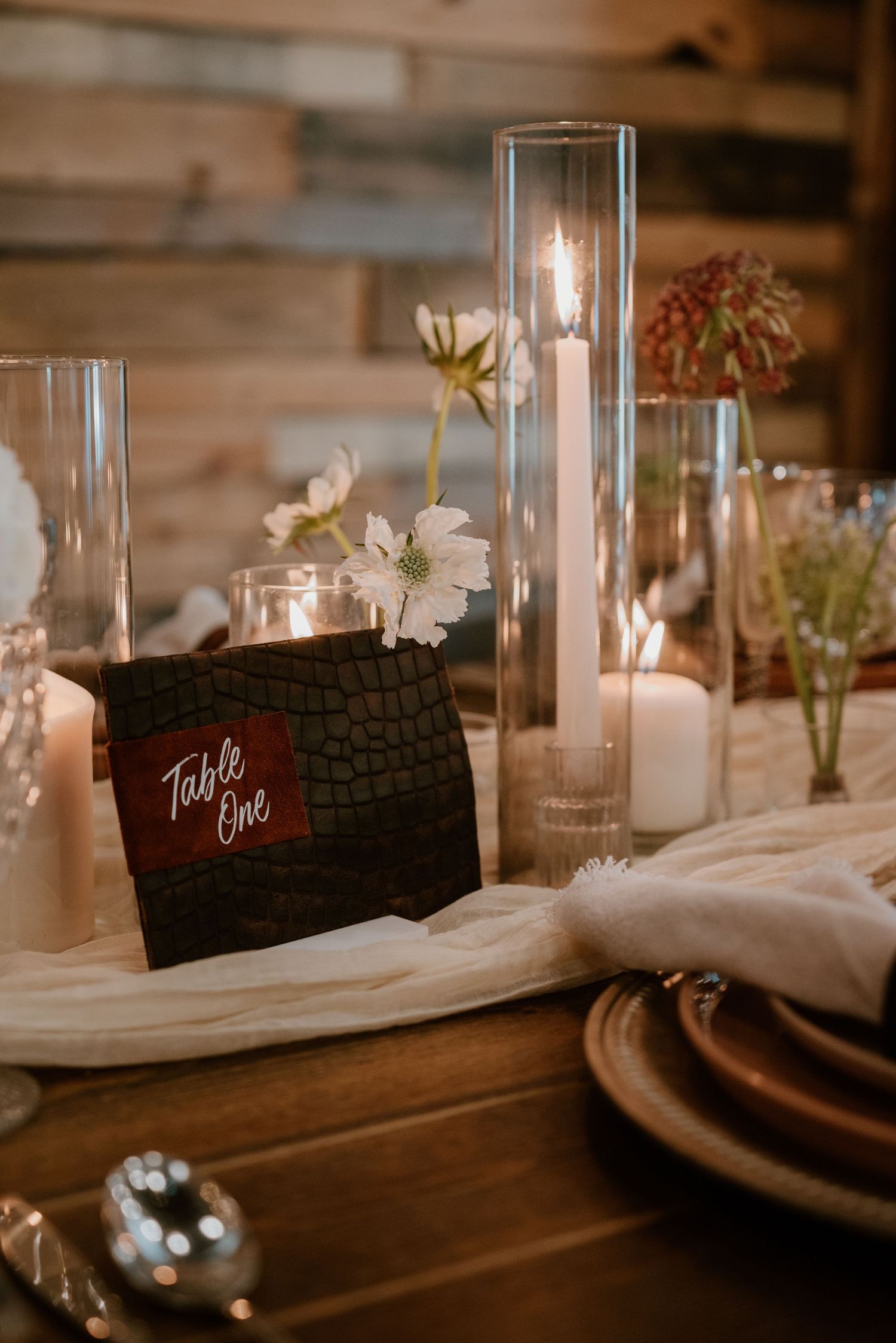 Elegant wedding table setting with glass candle holders and black name cards on white linens.