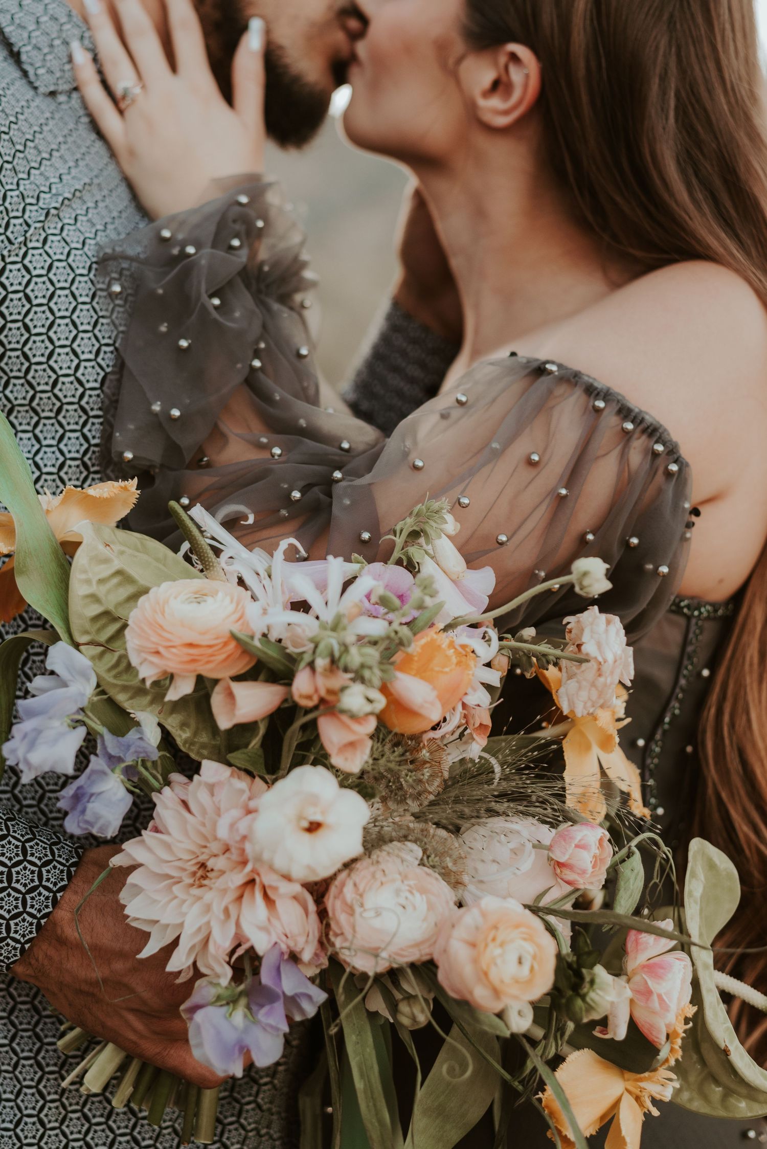 Close-up of romantic moment with pastel floral bouquet in foreground.