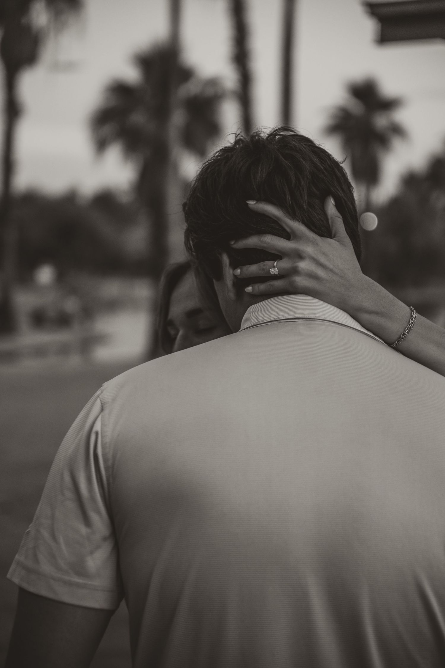 Dark silhouettes embracing against a sunset backdrop with palm trees.