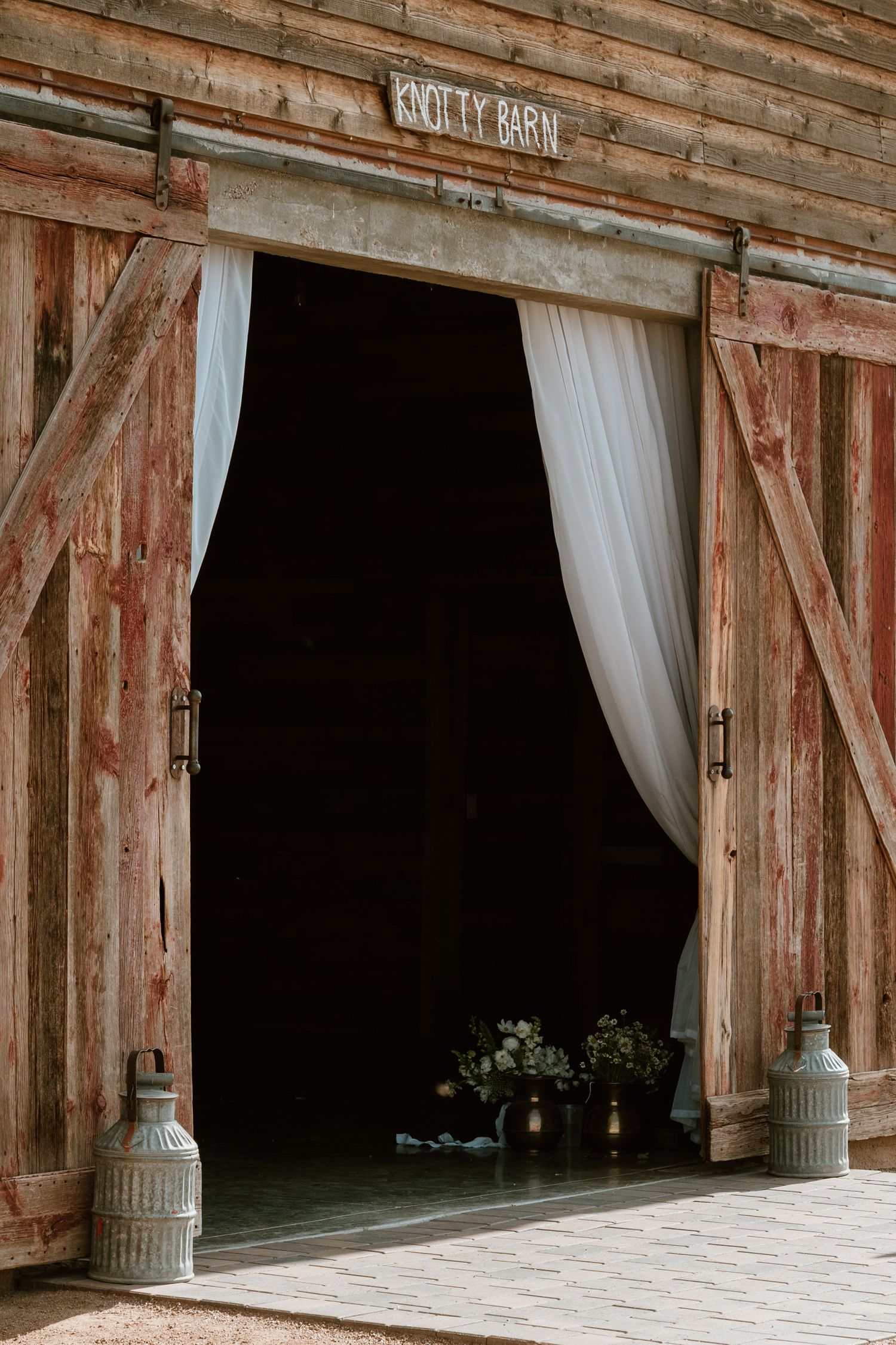 Rustic wooden barn with white curtained openings and weathered siding.