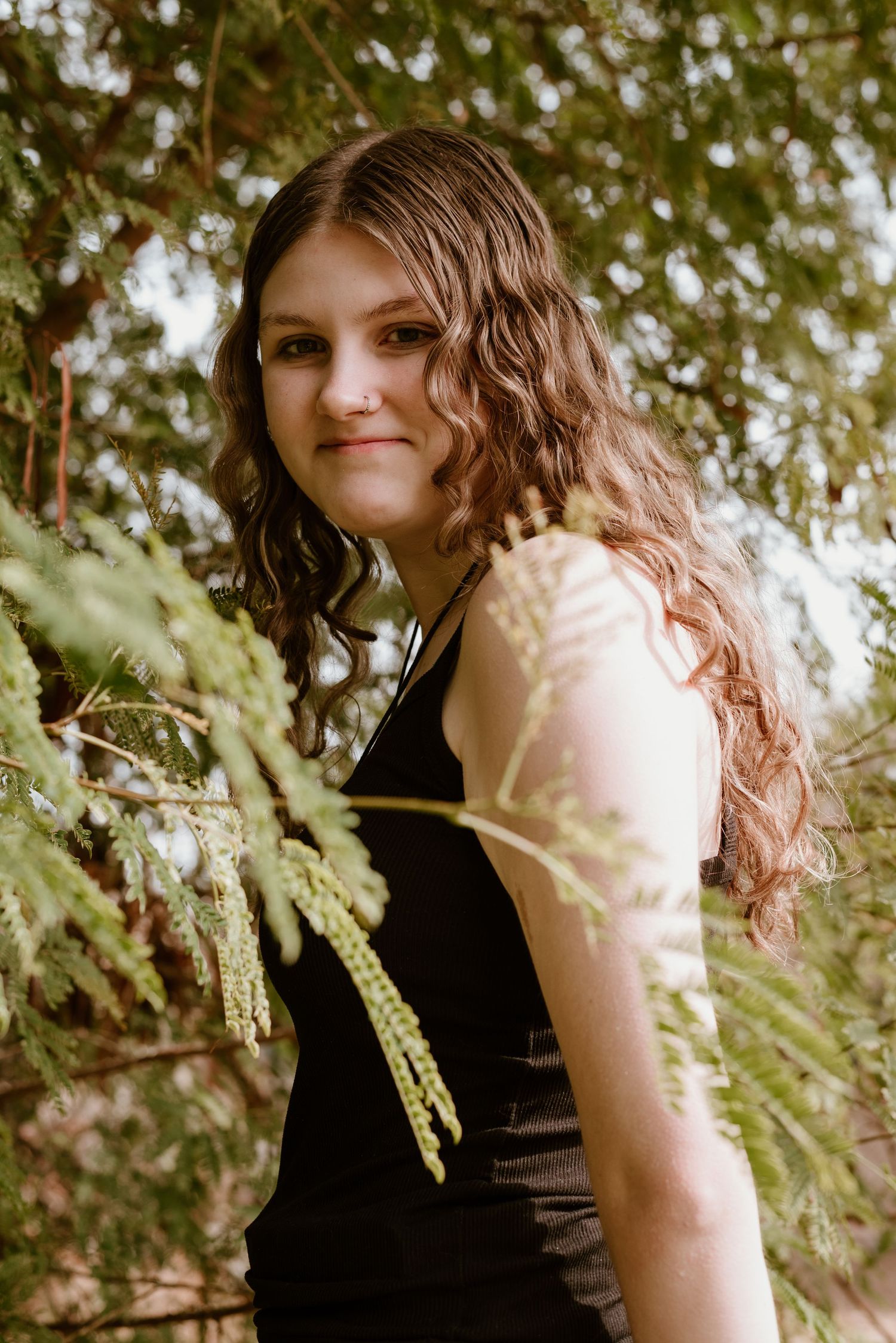 Portrait style photo with dappled sunlight filtering through pine branches in background.