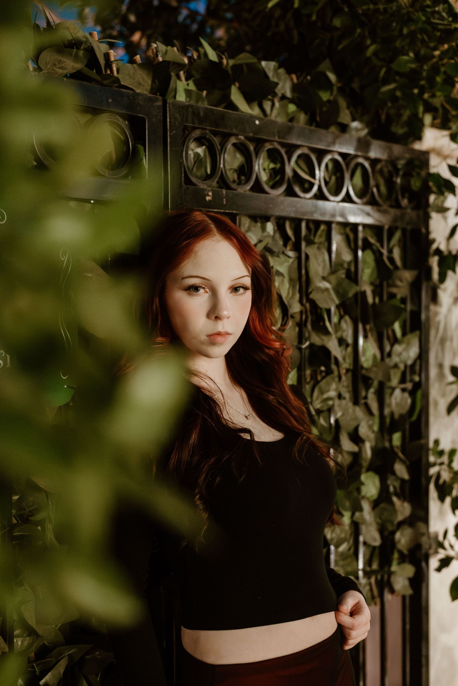 Fashion portrait against an ornate metal gate with lush greenery.