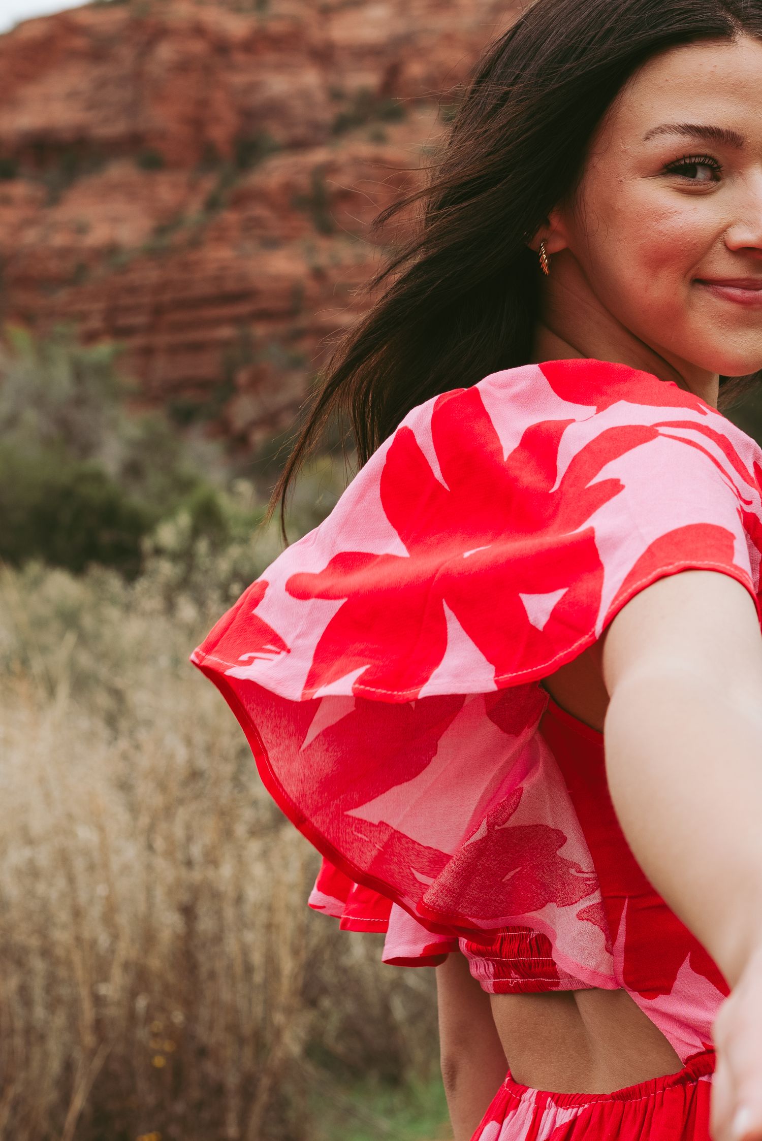 Vibrant red floral dress flowing in the wind against desert rock backdrop.