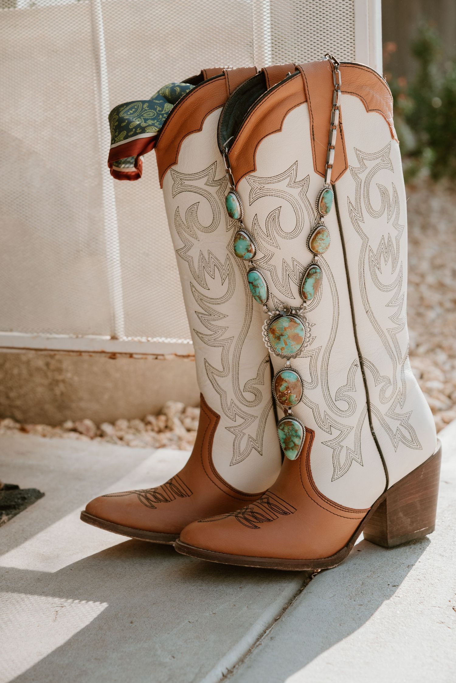 White and brown western boots adorned with turquoise accents on concrete floor.
