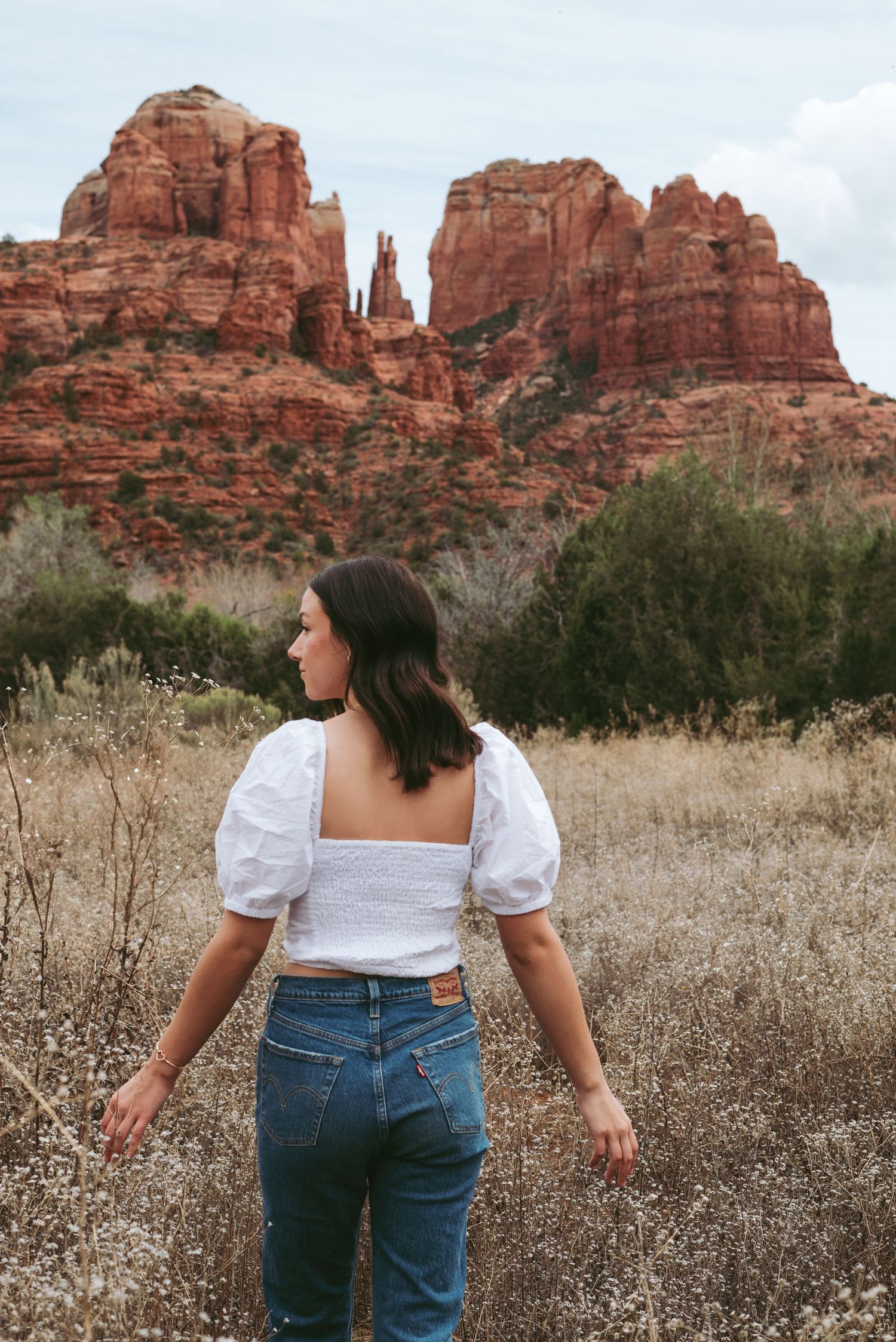 Person in white top and jeans looking at red rock formations in Sedona.