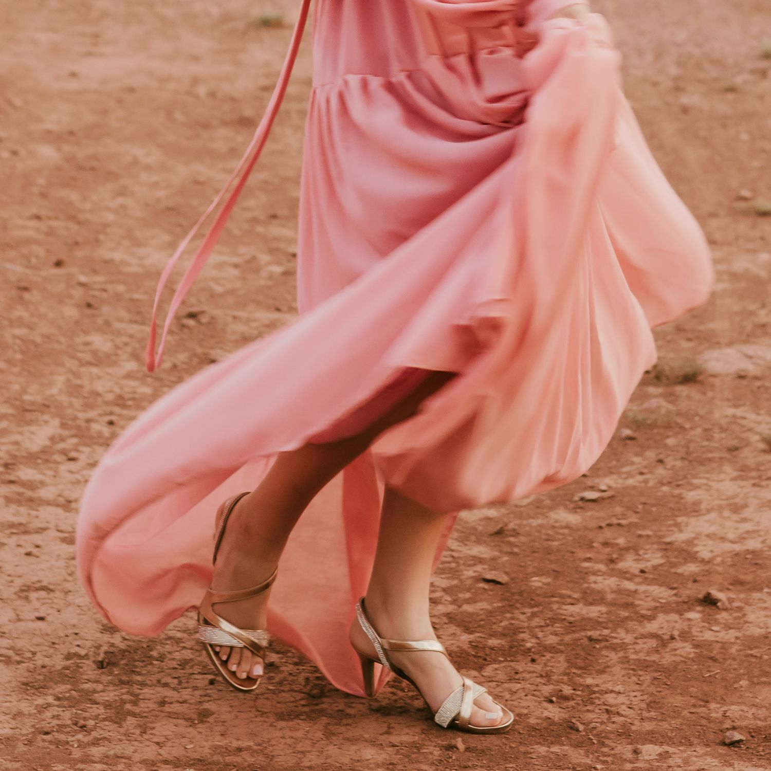 Pink flowy dress swirling around legs during desert photoshoot.