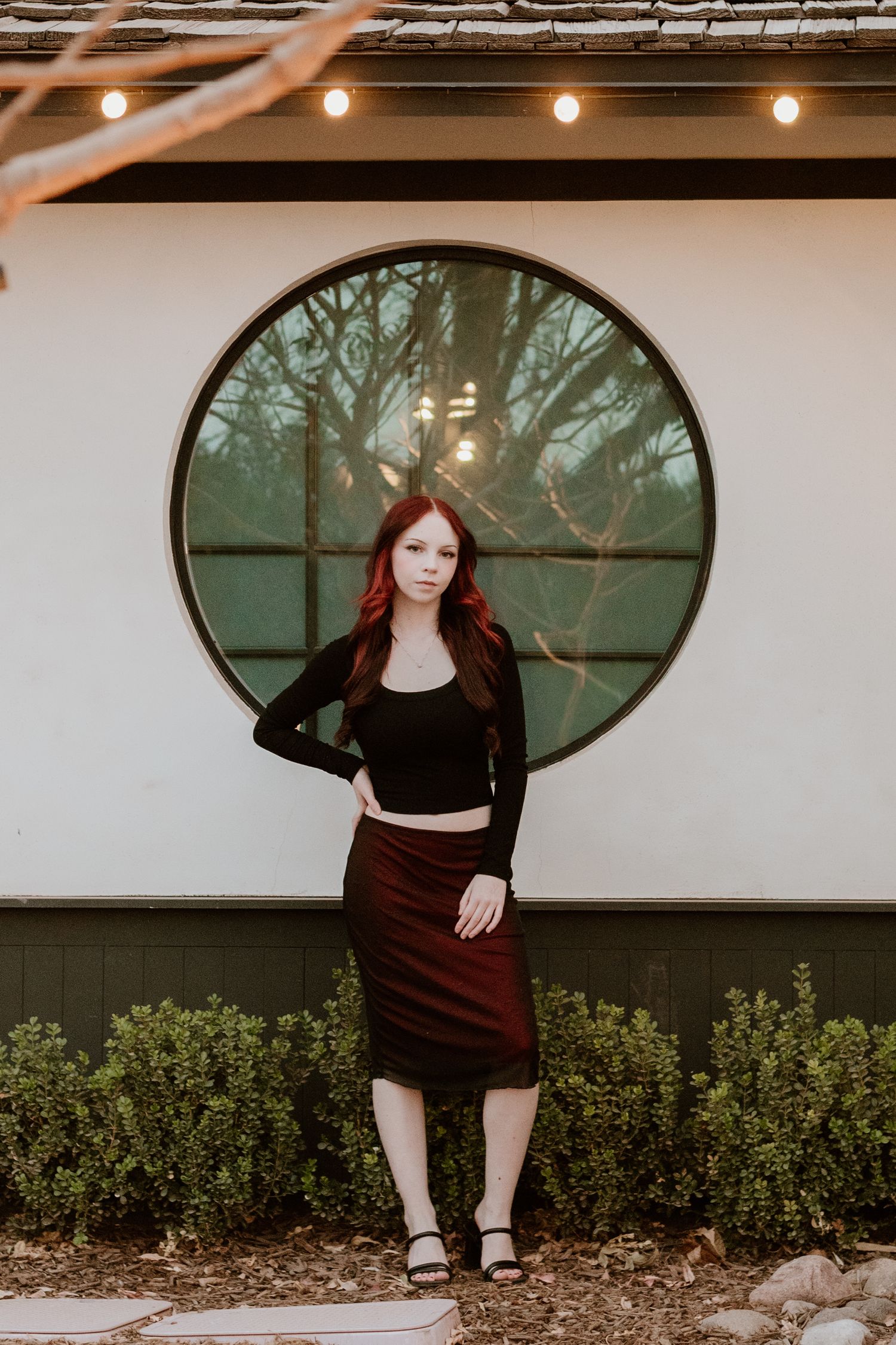 A stylish portrait in front of a circular window with moody forest backdrop.