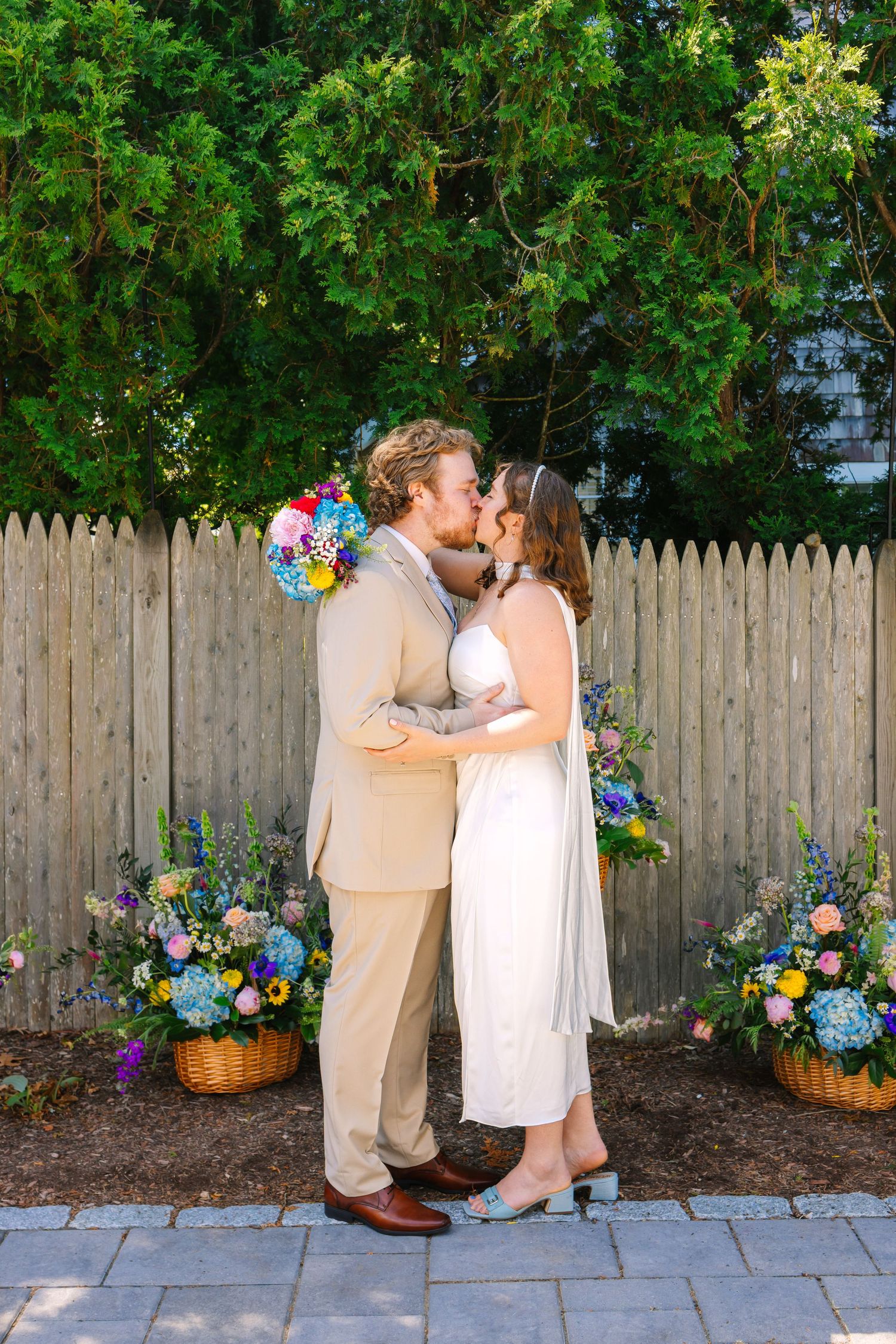Bride and Groom sharing a first kiss by colorful florals at backyard intimate elopement in Harwich Port Cape Cod Massachusetts