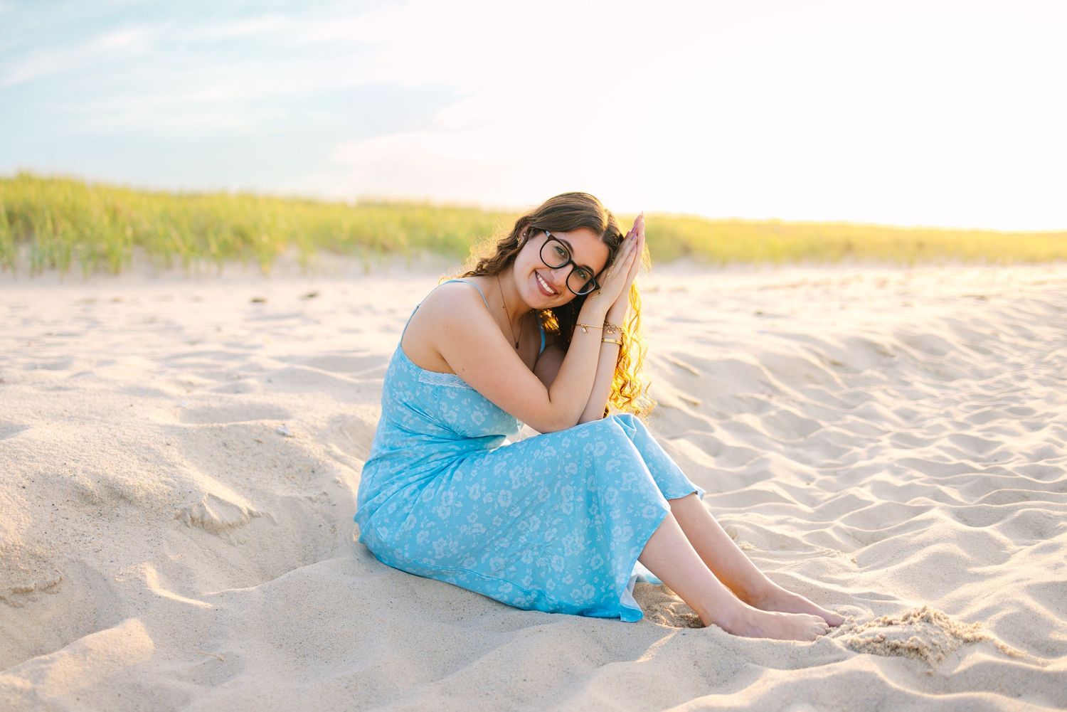 A high school senior sitting by the sand dunes during sunset golden hour for Cape Cod senior portraits at Scusset Beach in Sagamore, MA