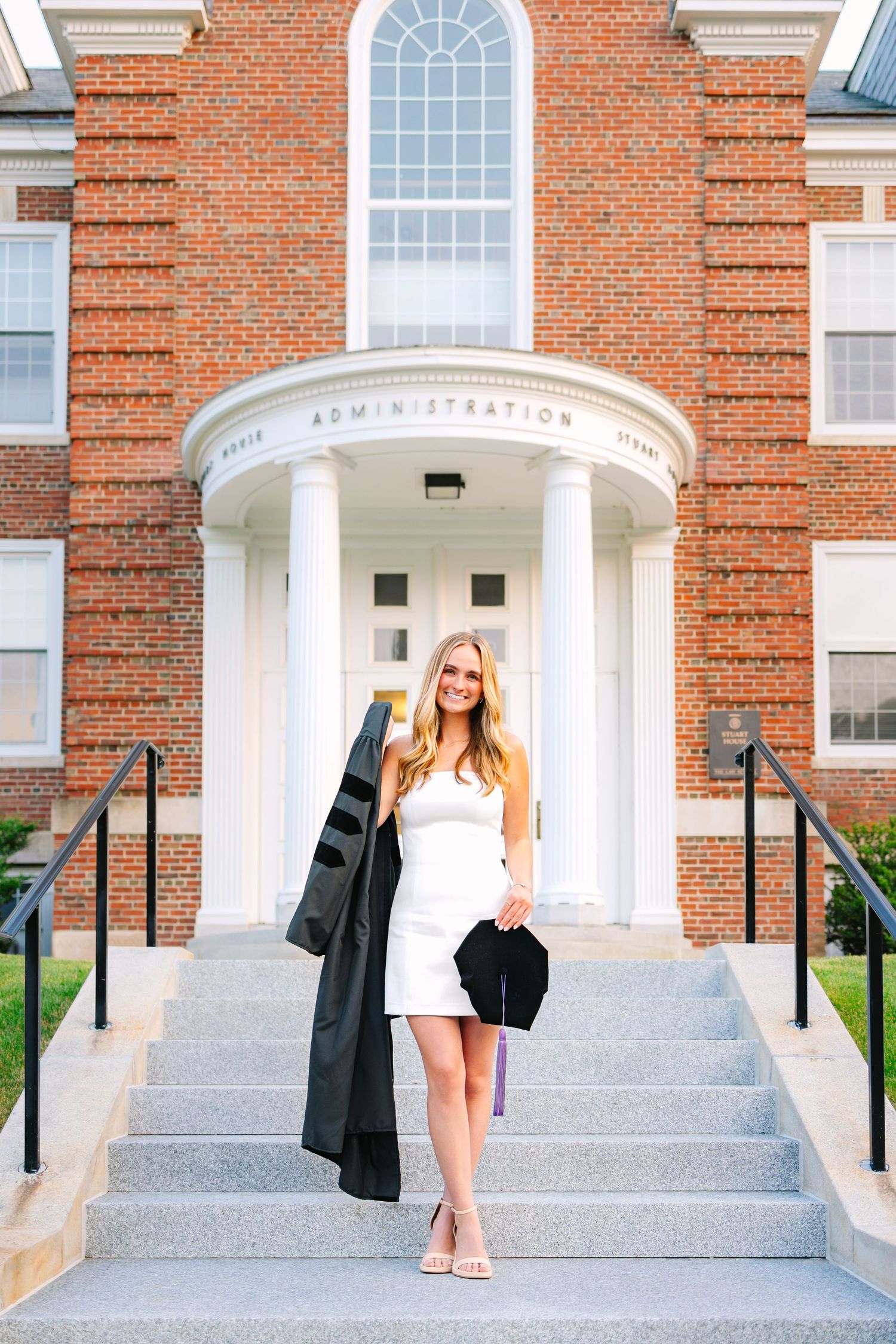 A college graduate posing in front of school building for graduation photos holding cap and gown at Boston College Law School in Newton, MA