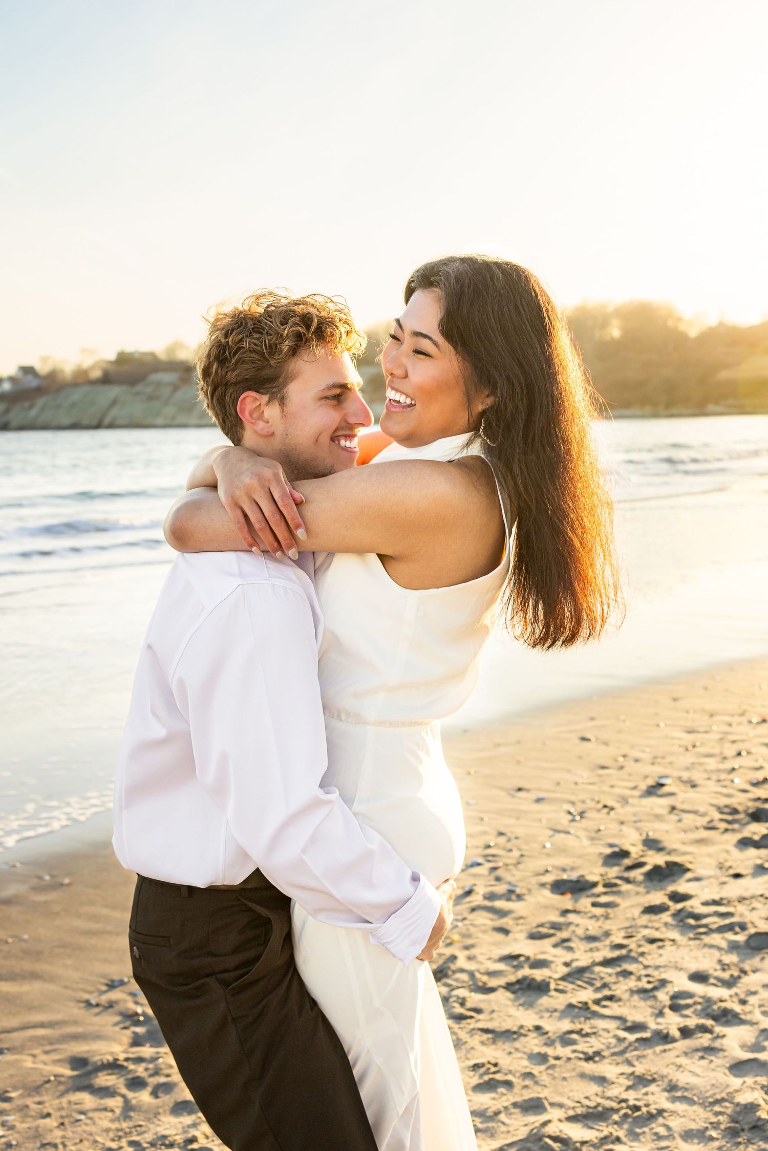 A couple candidly embraces during engagement session during sunset golden hour at Second Beach in Newport, Rhode Island