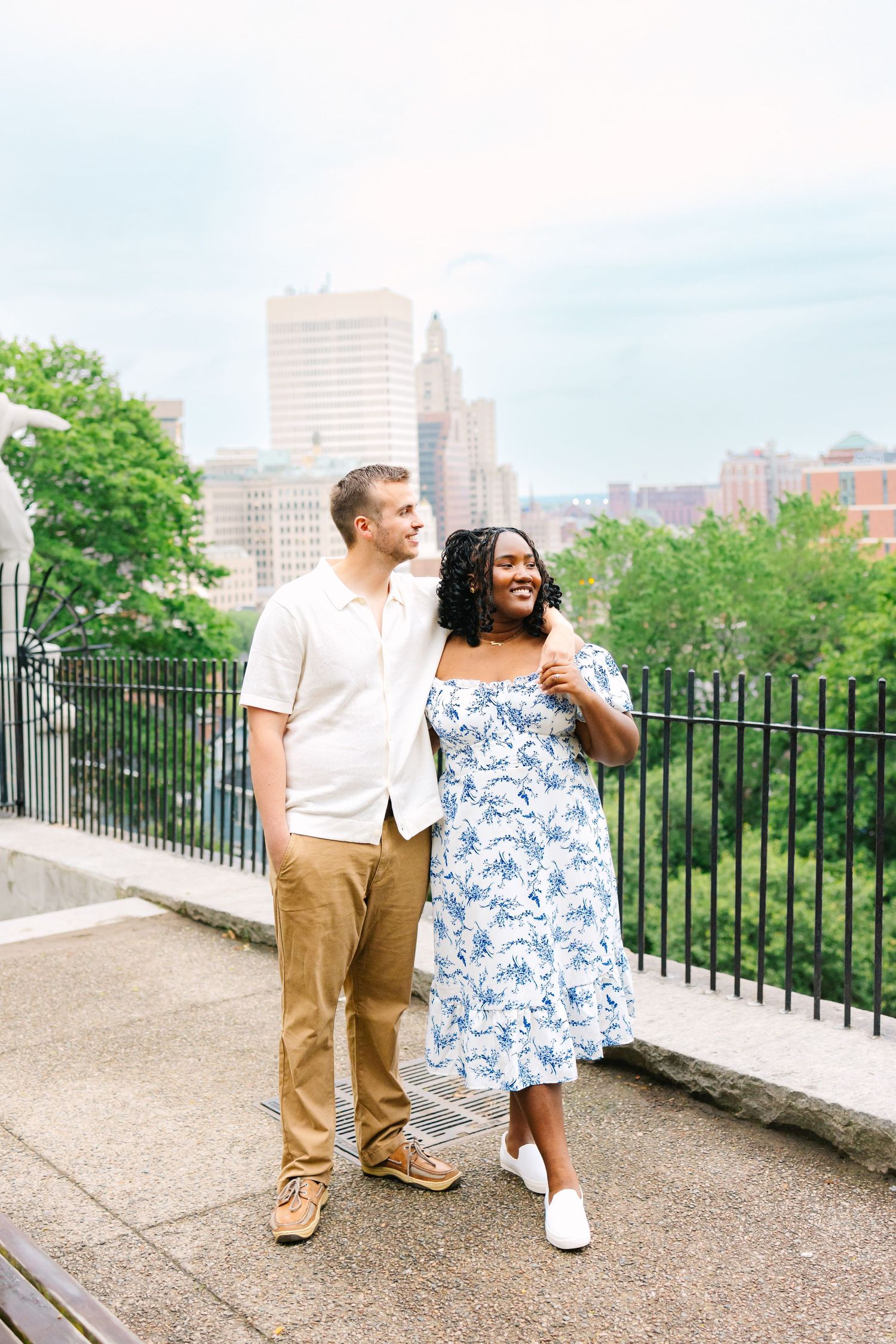 Couple poses lovingly by the Providence city skyline in Rhode Island for engagement photos
