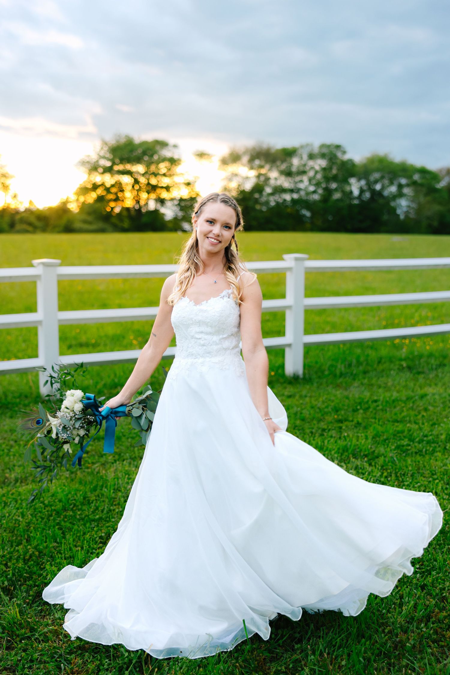 A bride wearing a wedding dress flows elegantly in a green field at sunset with white fence in background during backyard wedding in CT