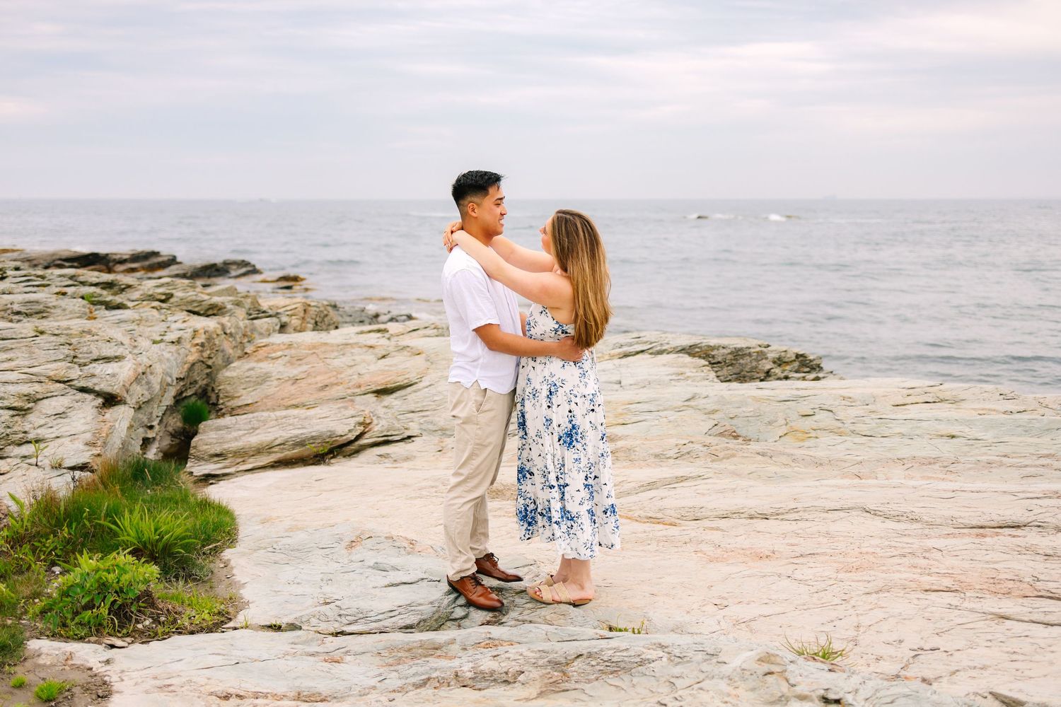 Couple embracing on rocky coastal shoreline with ocean backdrop for engagement photos on Ocean Drive in Newport Rhode Island