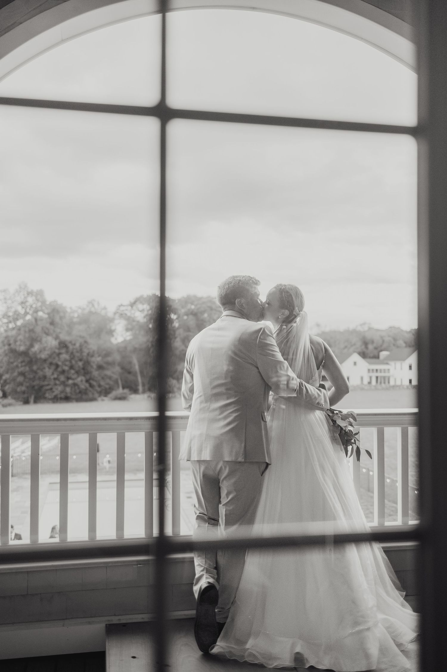 A romantic couple embraces on a covered porch overlooking a scenic landscape, captured in black and white photography backyard wedding CT