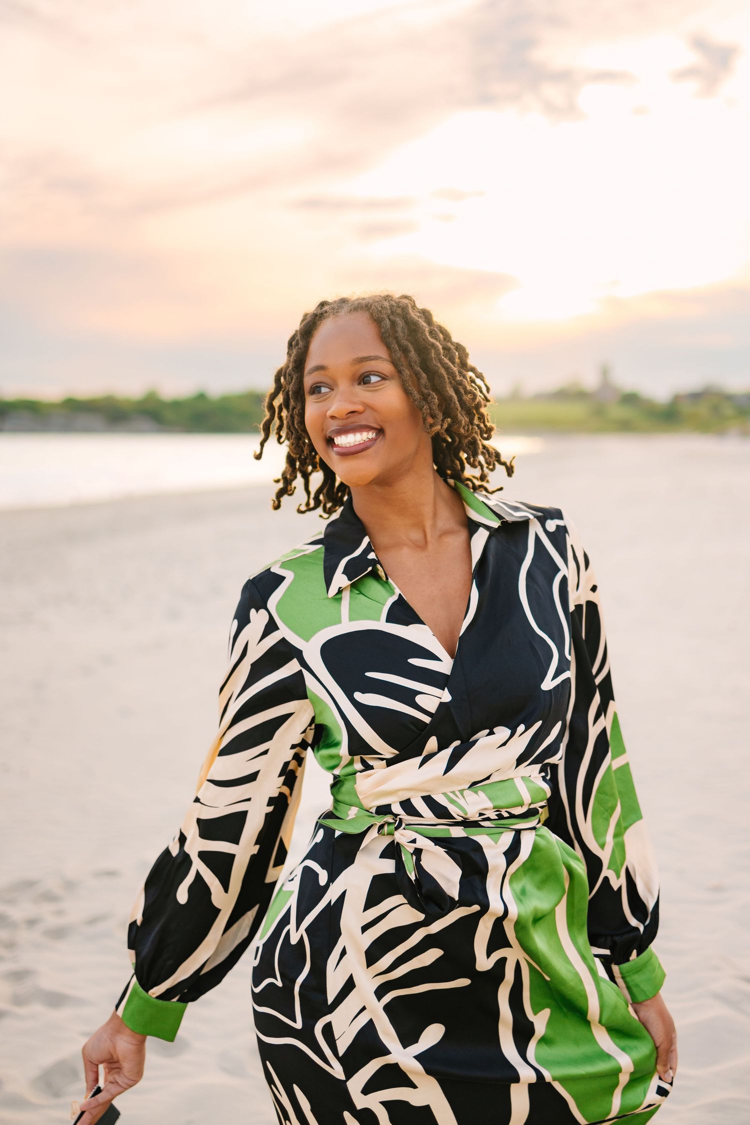 A college grad walking on the sandy beach for graduation photos at sunset golden hour at Second Beach in Newport Rhode Island Salve Regina