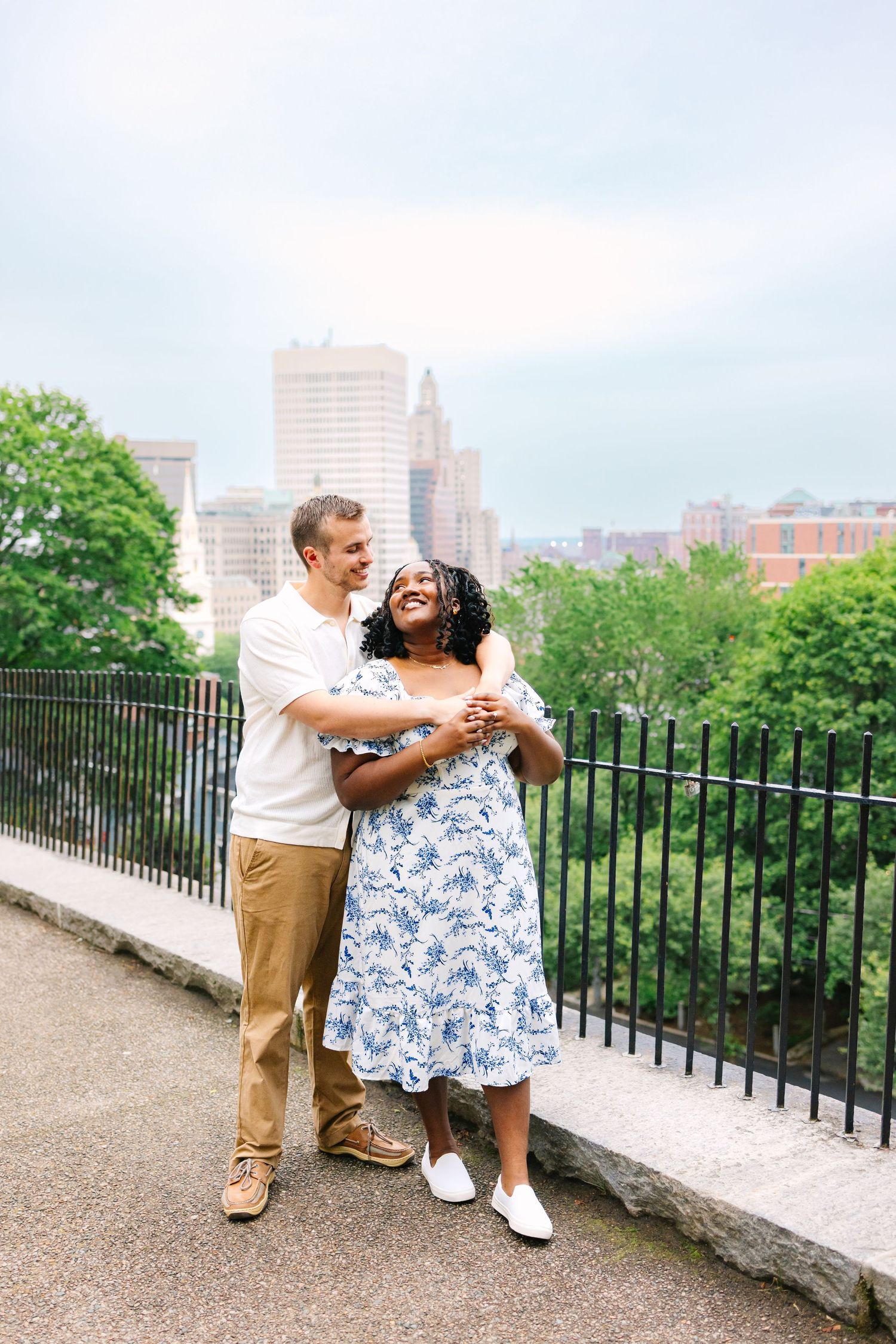 A couple shares a sweet romantic moment at a scenic urban overlook with city buildings visible in Providence Rhode Island after proposal