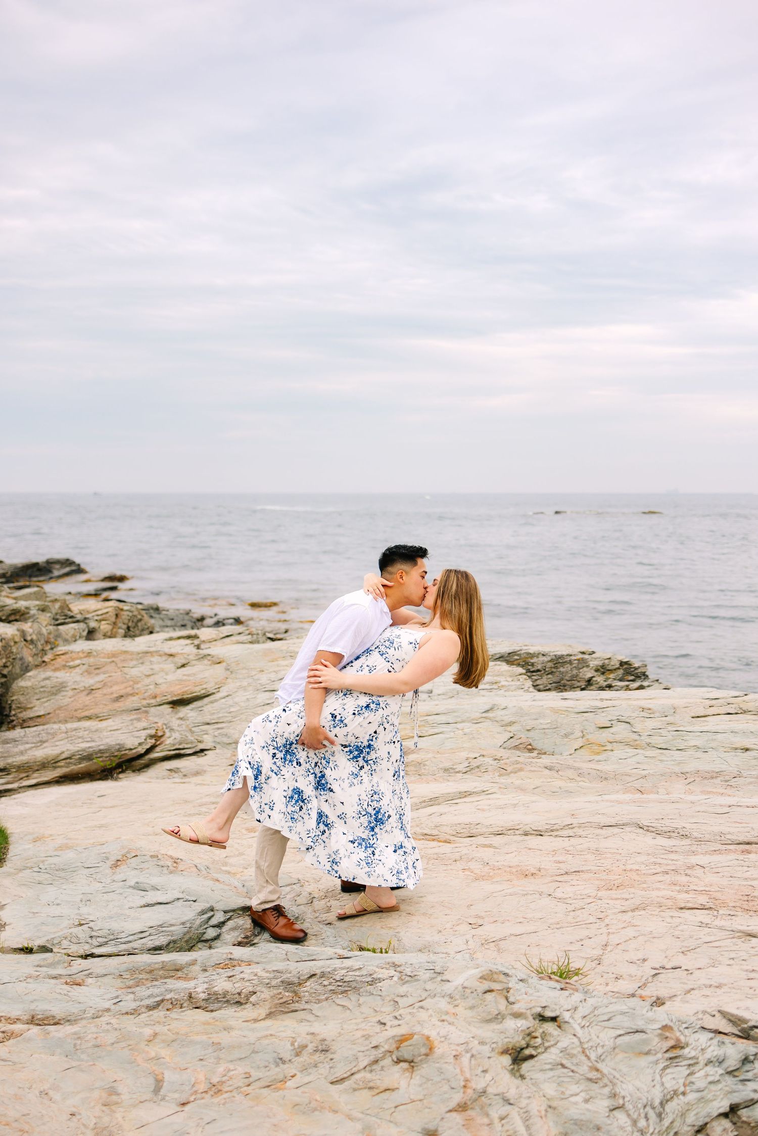 A couple dances romantically on coastal rocks overlooking the ocean under an overcast sky on Ocean Drive in Newport Rhode Island