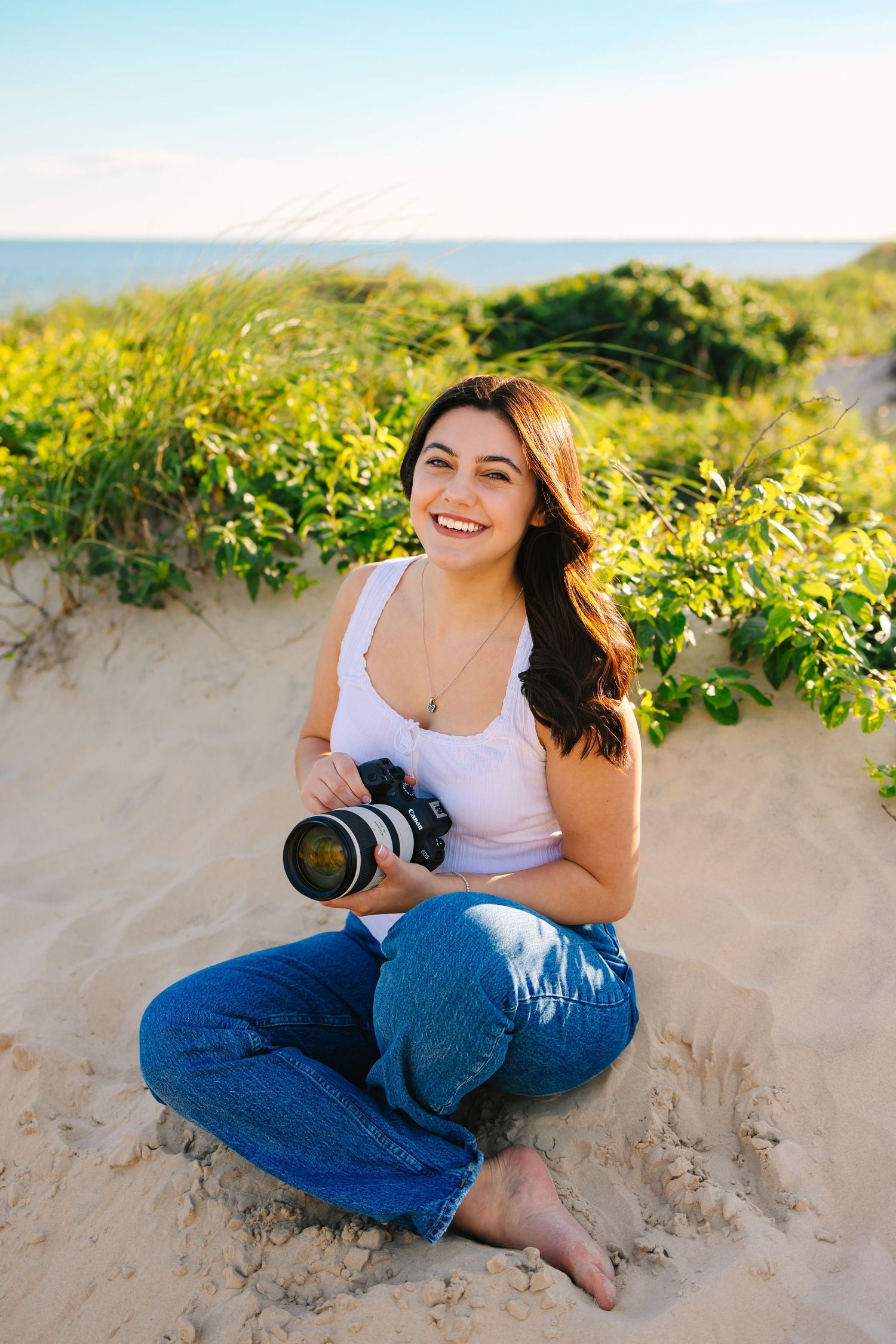 Photographer smiling holding camera by the sand dunes for branding photos at sunset golden hour at Horseneck Beach in Westport, MA