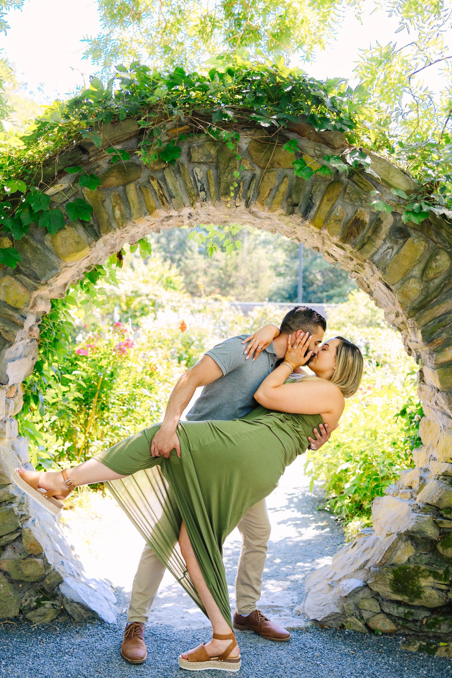 A romantic moment captured under a stone archway covered in vines during a sunny day.
