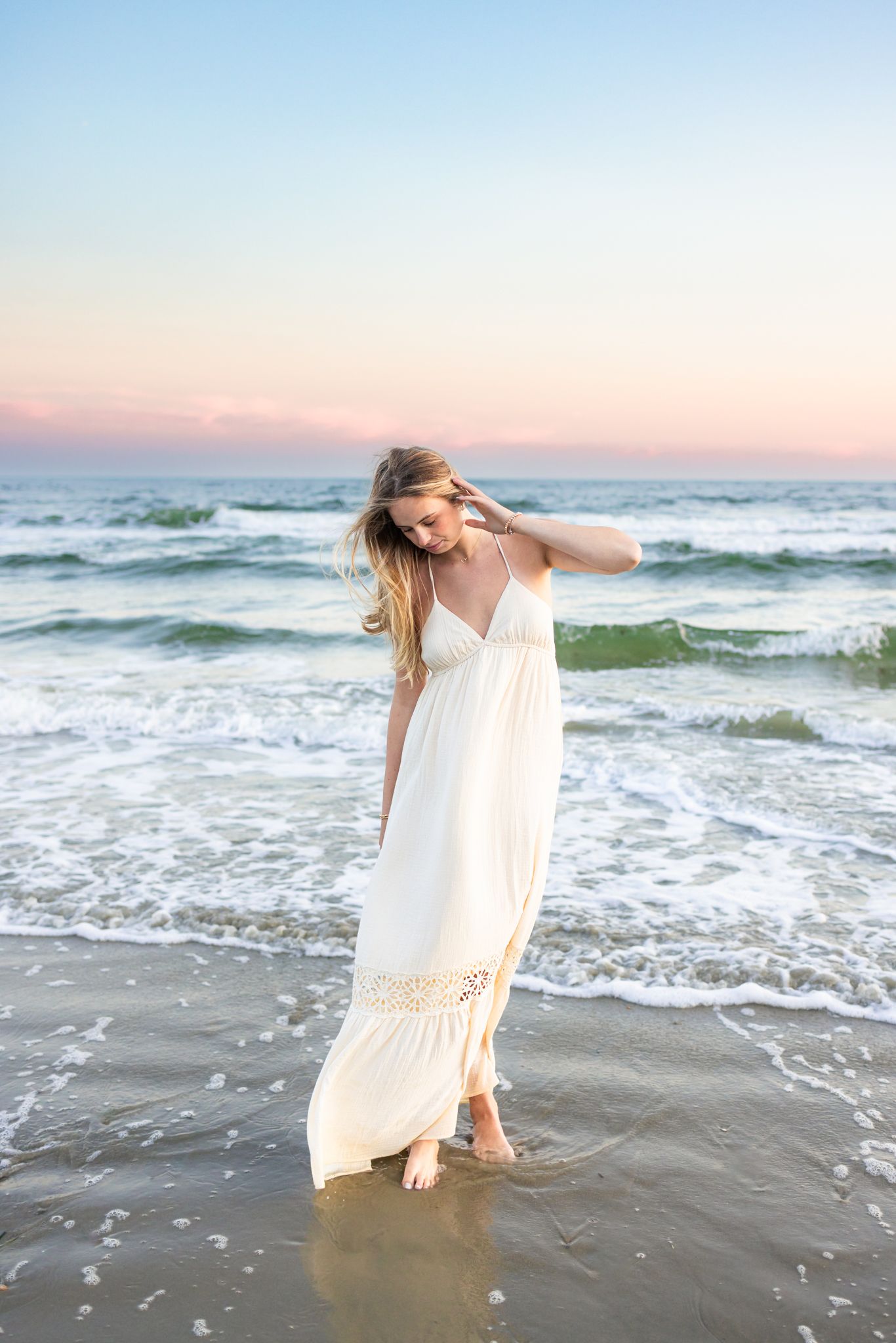 A high school senior candidly walking by the shoreline at sunset golden hour for senior photos at Horseneck Beach in Westport, Massachusetts