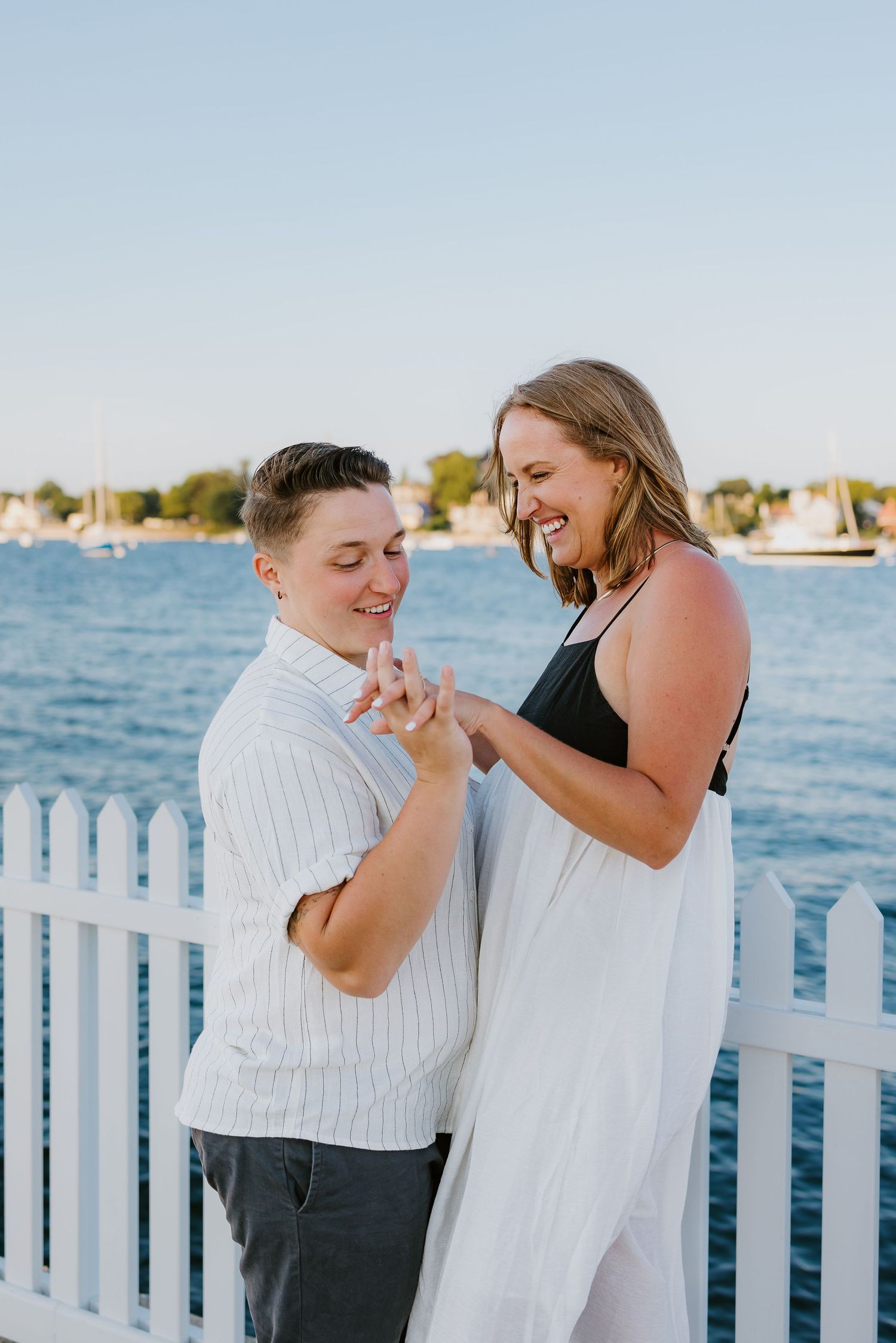 A happy couple shares a joyful moment together by a white picket fence overlooking a marina on a sunny day at Newport Harbor Island Resort